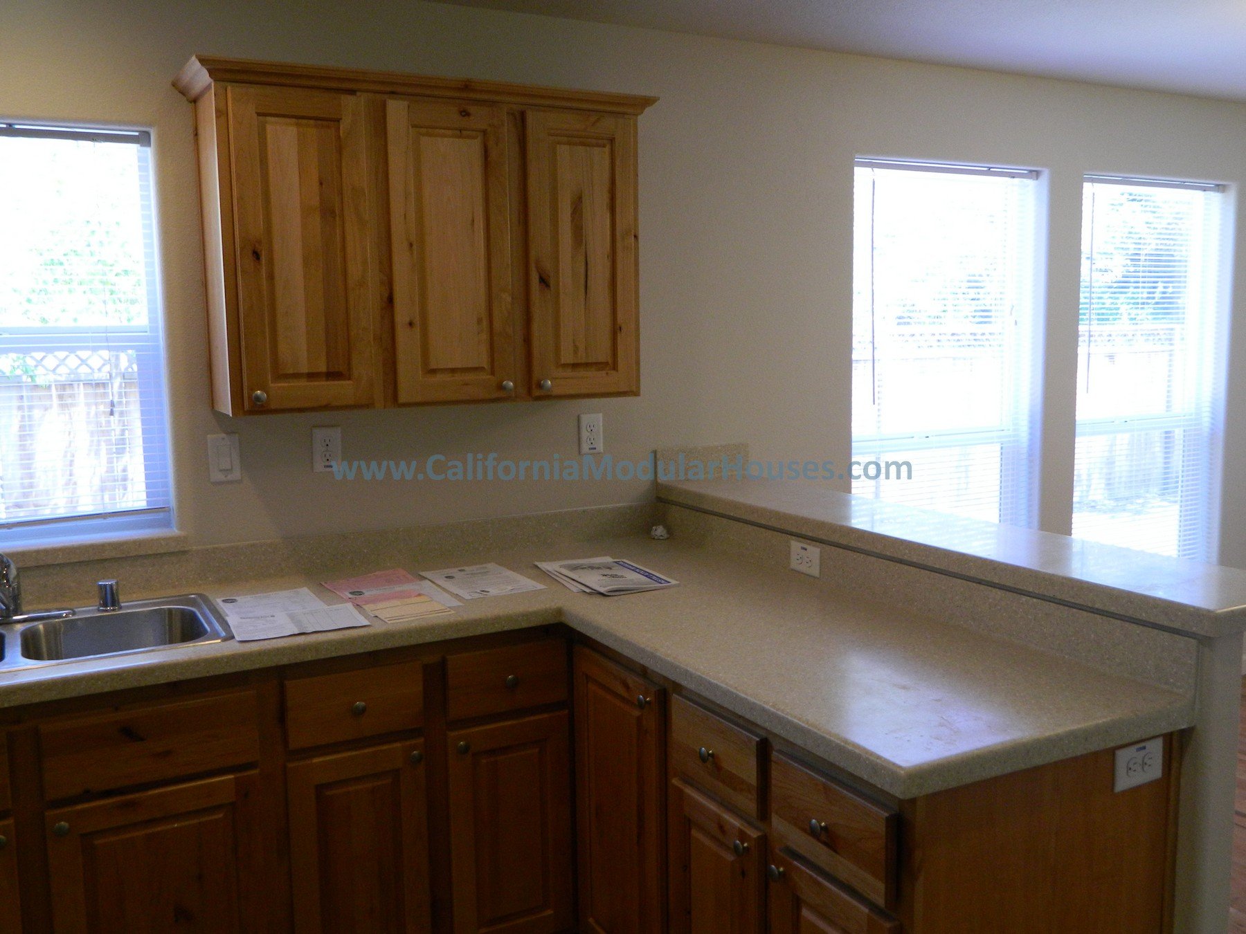 Kitchen with wooden cabinets, beige countertop, sink, and large windows with blinds.