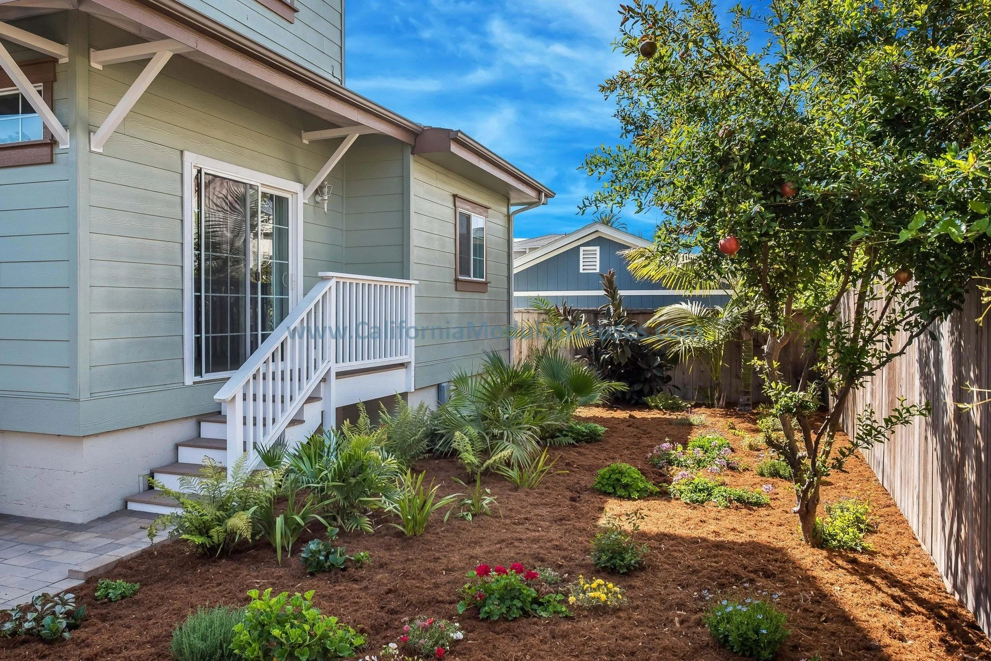 Backyard view of a sage green, brown trim prefab modular, two-story home. White door, white railing.