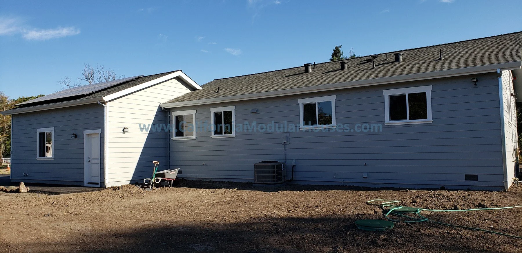 Side of a California Accessory Dwelling Unit with light gray siding and windows, Prefab modular ADU with attached single car garage.  Contra Costa County CA