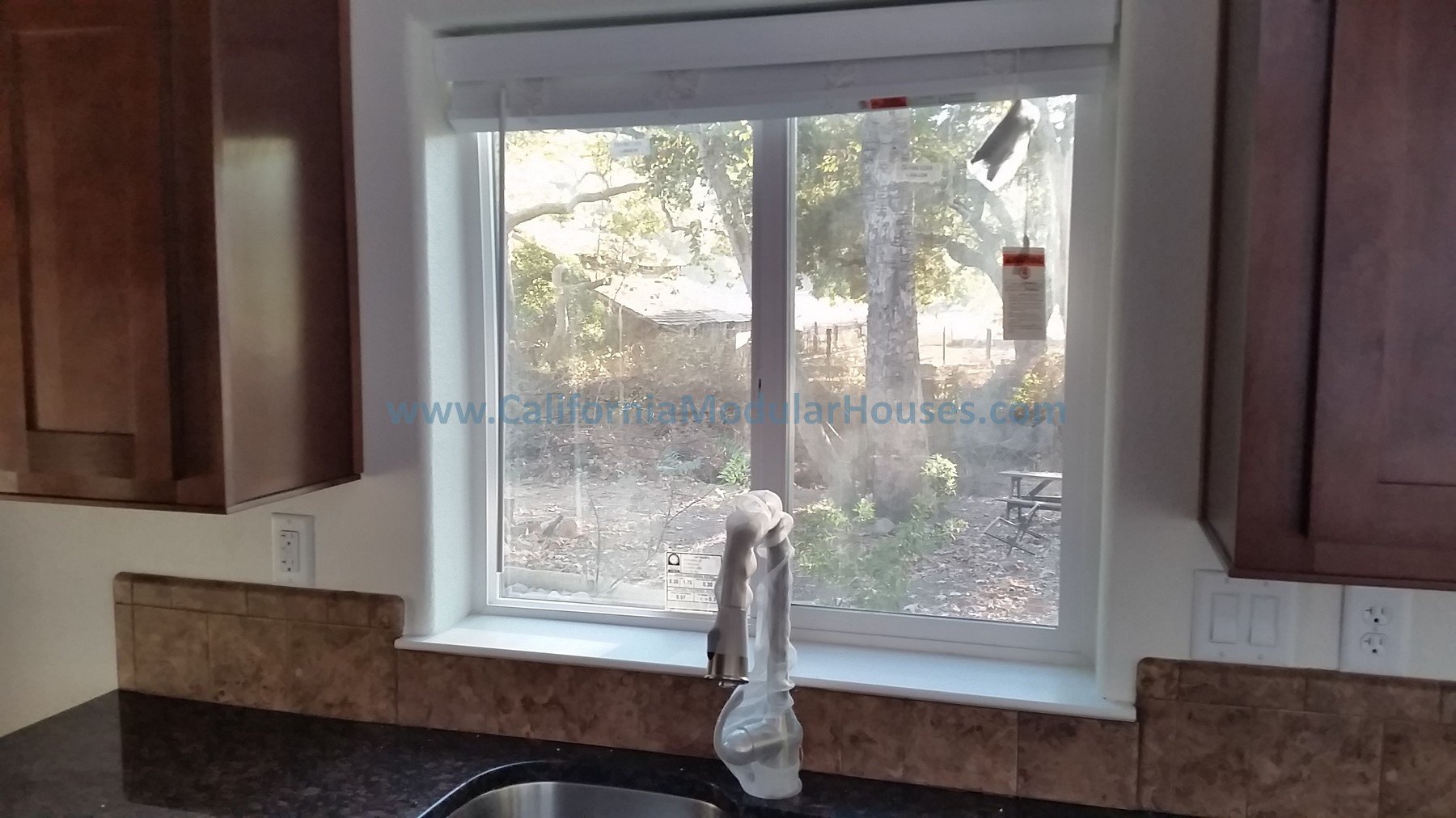 Kitchen window with a view of trees and a backyard, with a faucet and granite countertop in front.   Interior picture of Accessory Dwelling Unit Morgan Hill, Santa Clara County, CA  Modular ADU