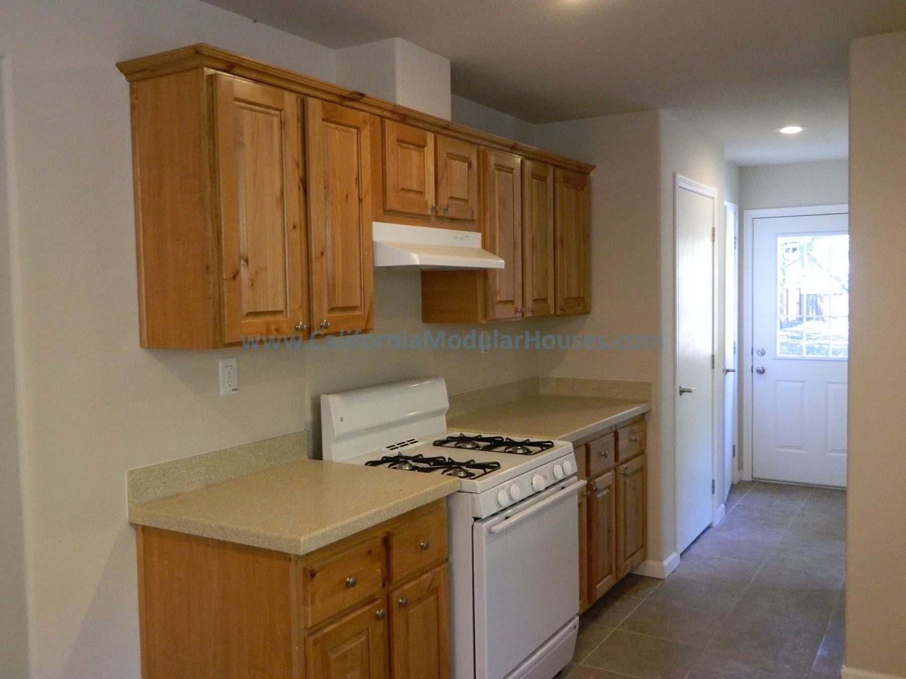 Kitchen with wooden cabinets, a white stove, and a door leading outside.