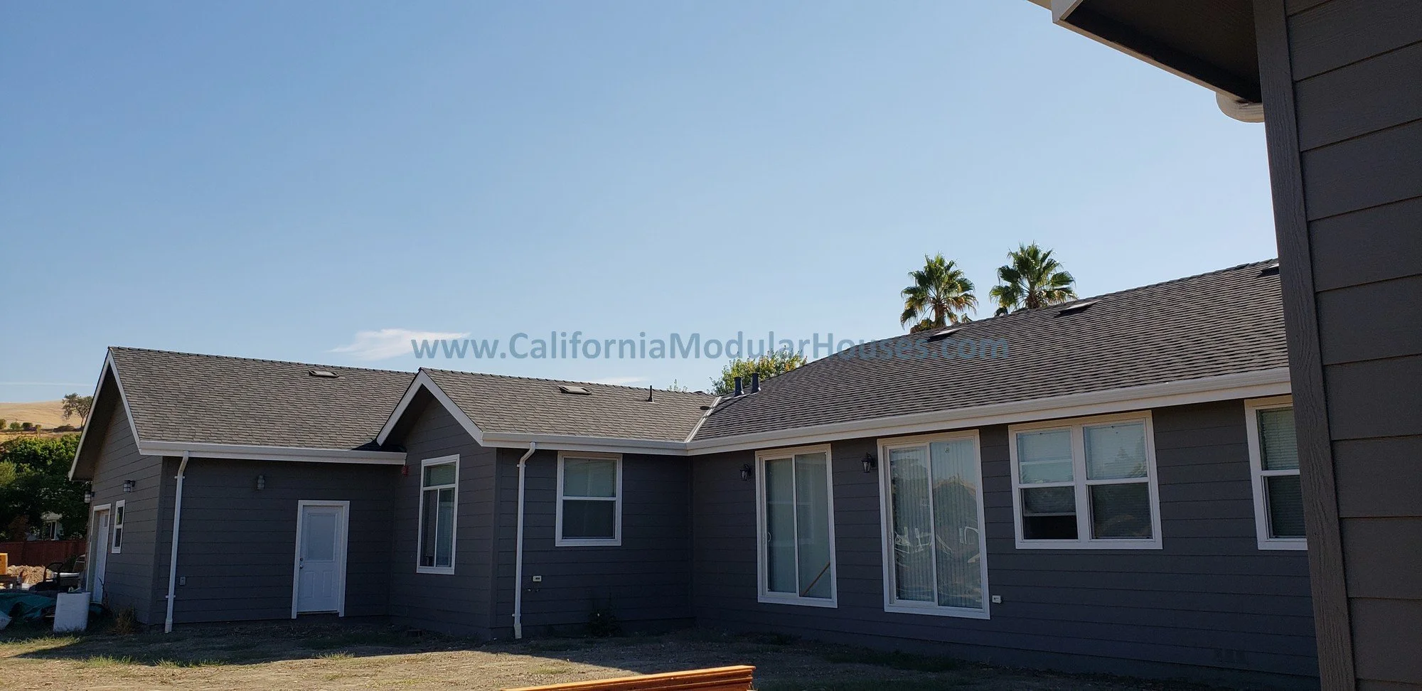 This Factory Built Home image shows many of the rear windows as well as a couple of doors of the home for egress.  Lots of natural light in this home and beautiful comp shingle roofing.  