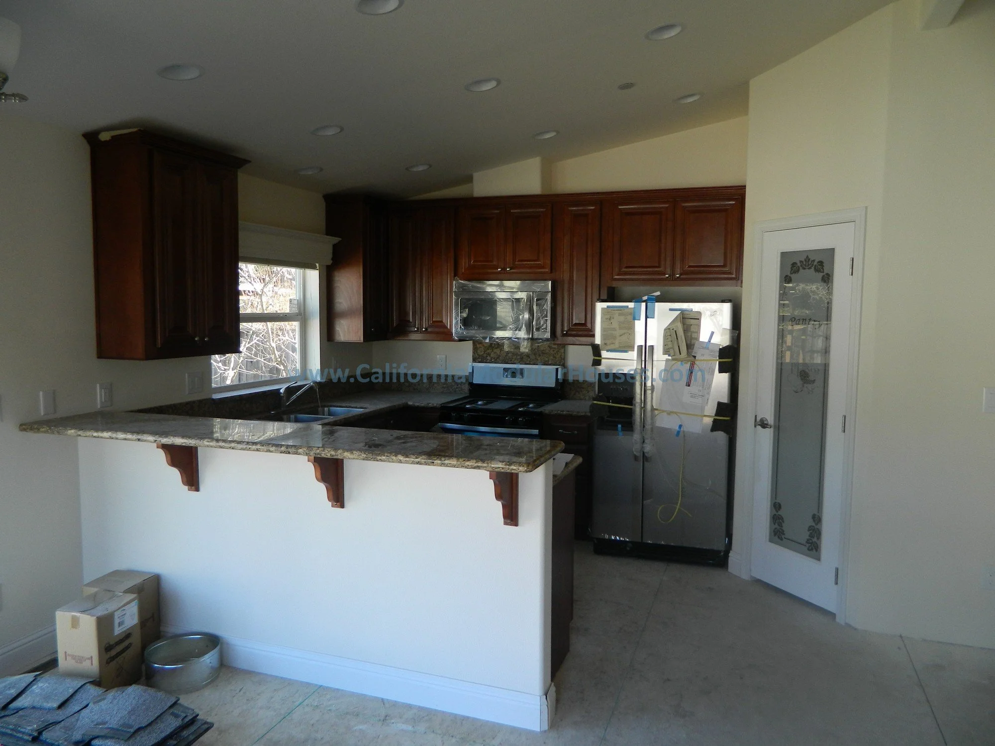 Kitchen with dark wood cabinets, granite countertops, stainless steel appliances, window with outdoor view, and a door with decorative glass panel.