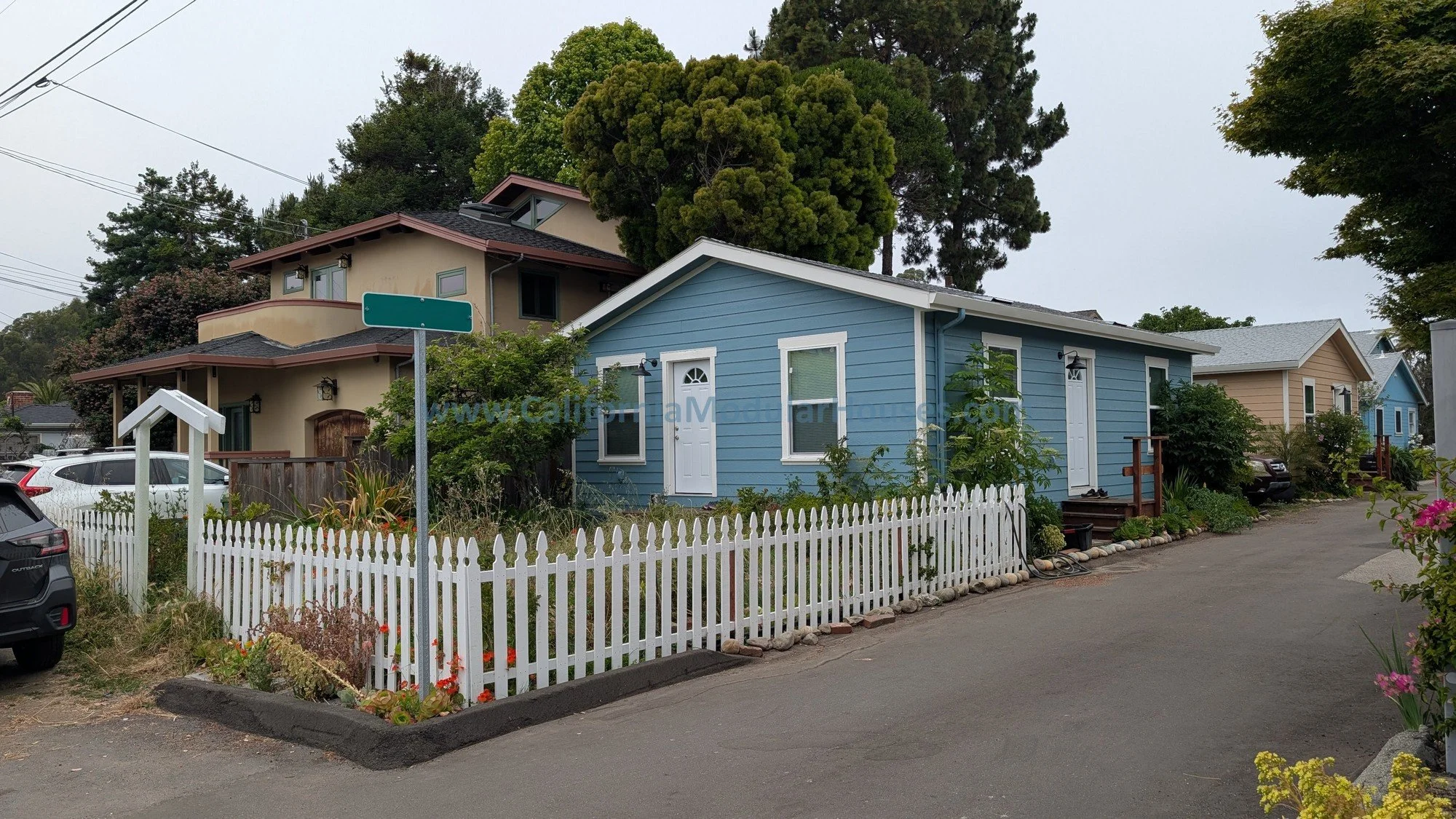 Colorful houses on a residential street with white picket fences, plants, and trees in California.