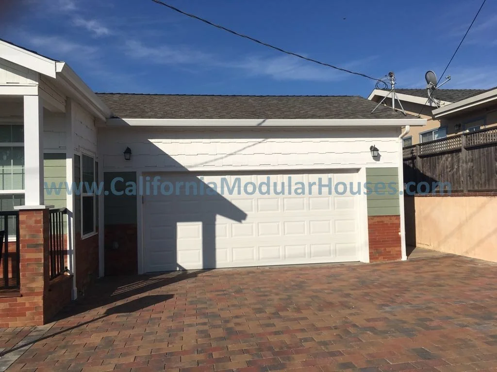 Front view of a modern house with a brick and white siding exterior, a garage door, and a paved driveway, under a partly cloudy sky.