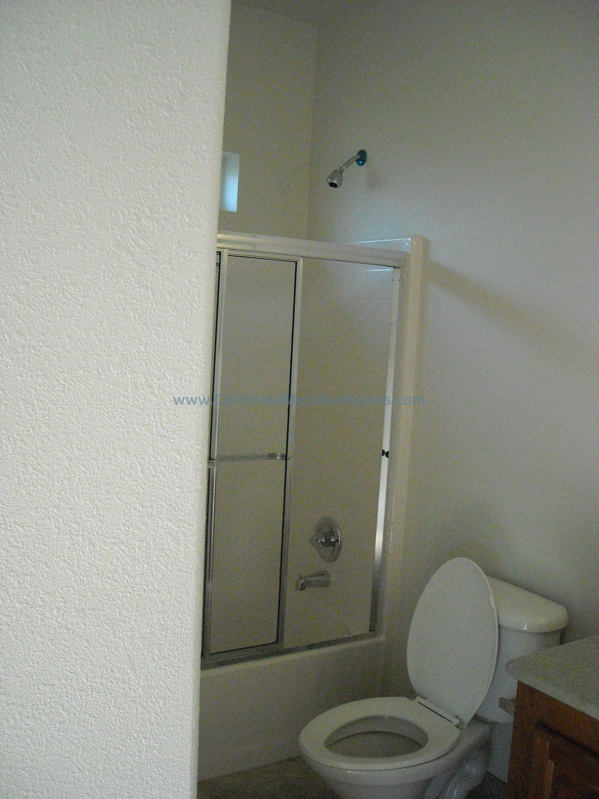Bathroom with a shower stall, toilet, and partial view of a wooden cabinet.  Factory Built Housing, Walker Basin, Kern County, CA.  