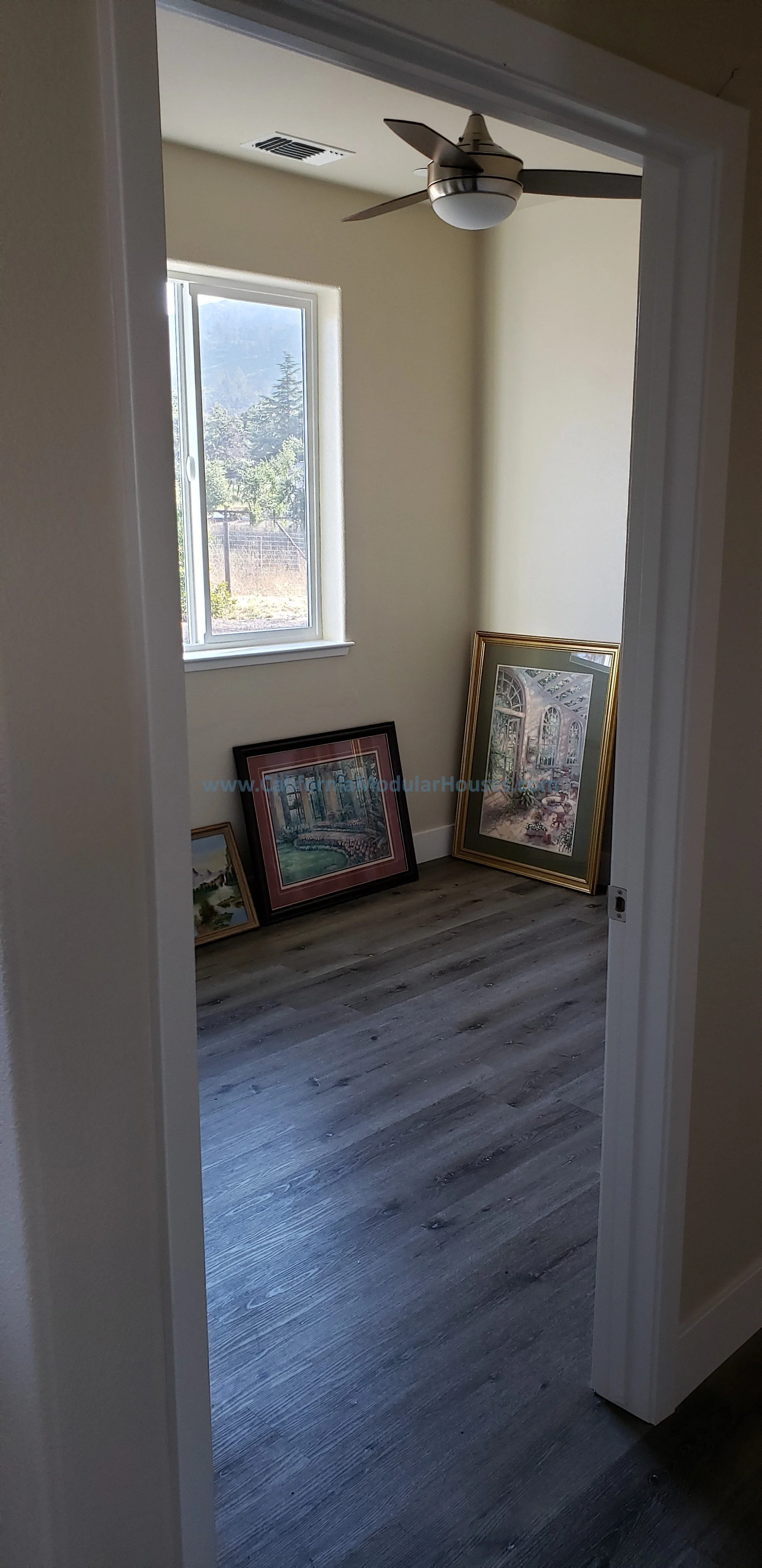 A small room with a window showing a landscape outside, a ceiling fan with a light, and three framed pictures leaning against the wall on the floor. Interior picture of Accessory Dwelling Unit Kenwood, Sonoma County, CA