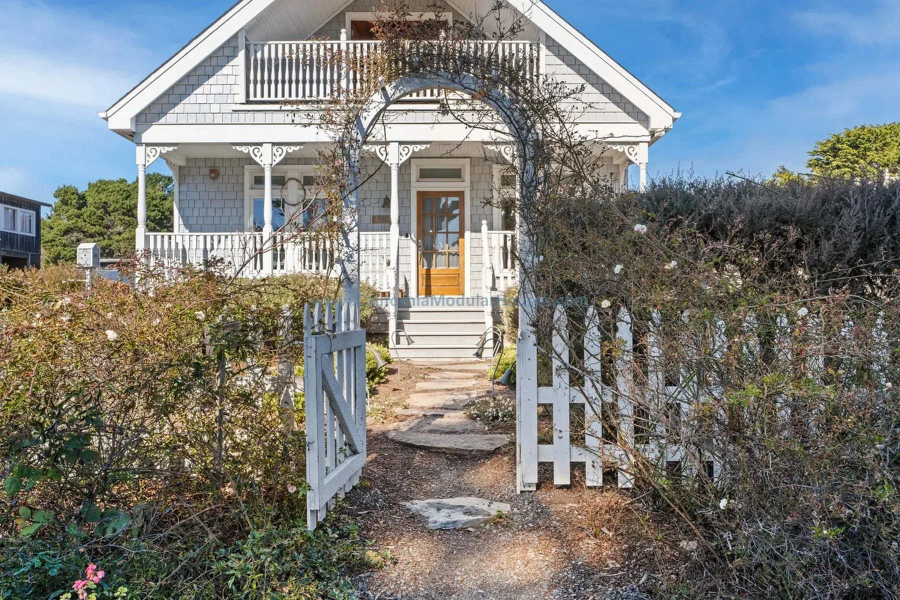 A white wooden house with a porch and stairs and a white picket gate at the front.  Cape Cod Modular Home.  Mendocino City, Mendocino County, CA.  Coastal Commission Review.  Historical Commission Review.  