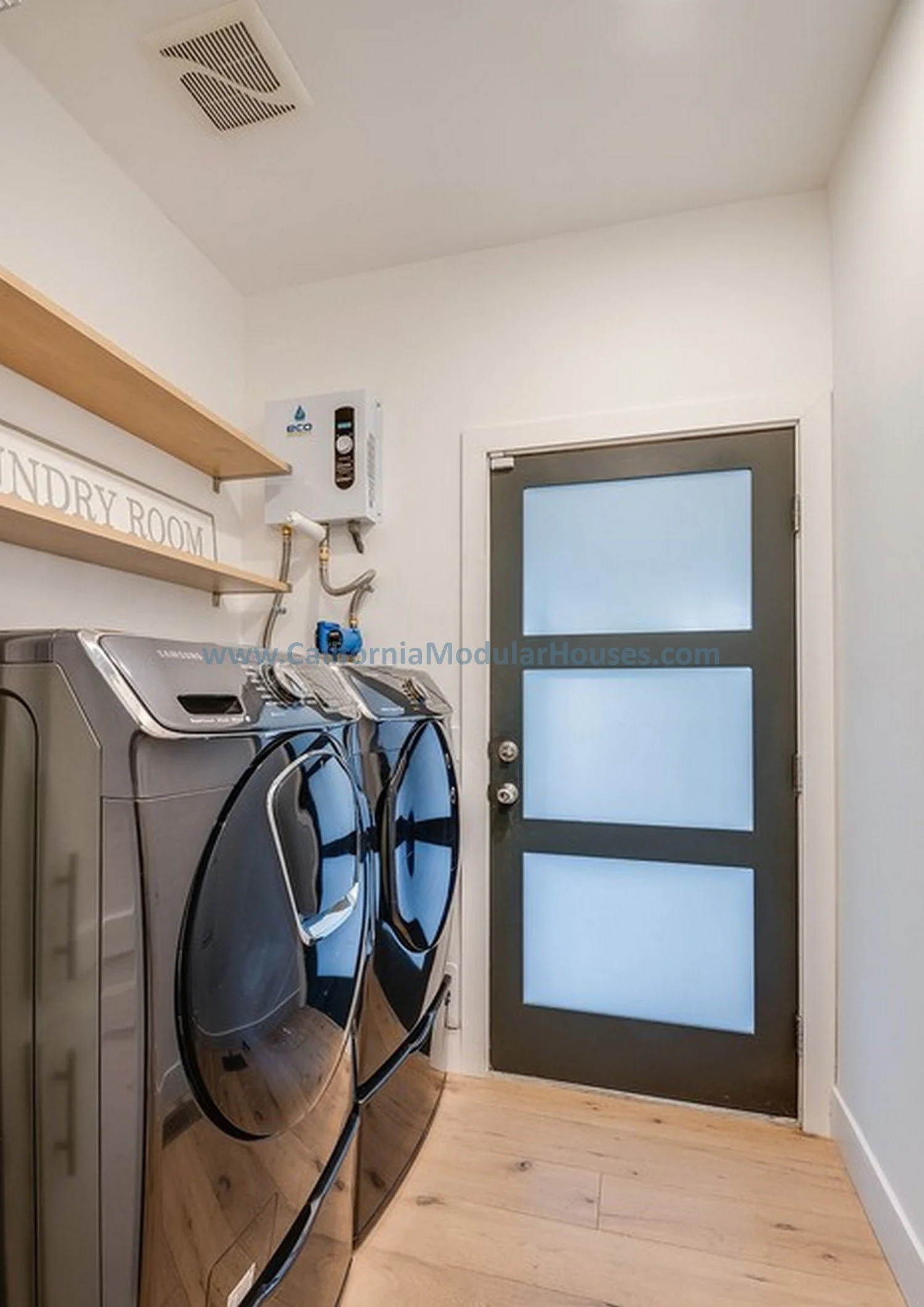 Laundry room with front-loading washer and dryer, a wall-mounted water heater, wooden shelves, and a door with frosted glass panels.  Toluca Lake, Los Angeles, Los Angeles County, California. Factory Built Housing.  
