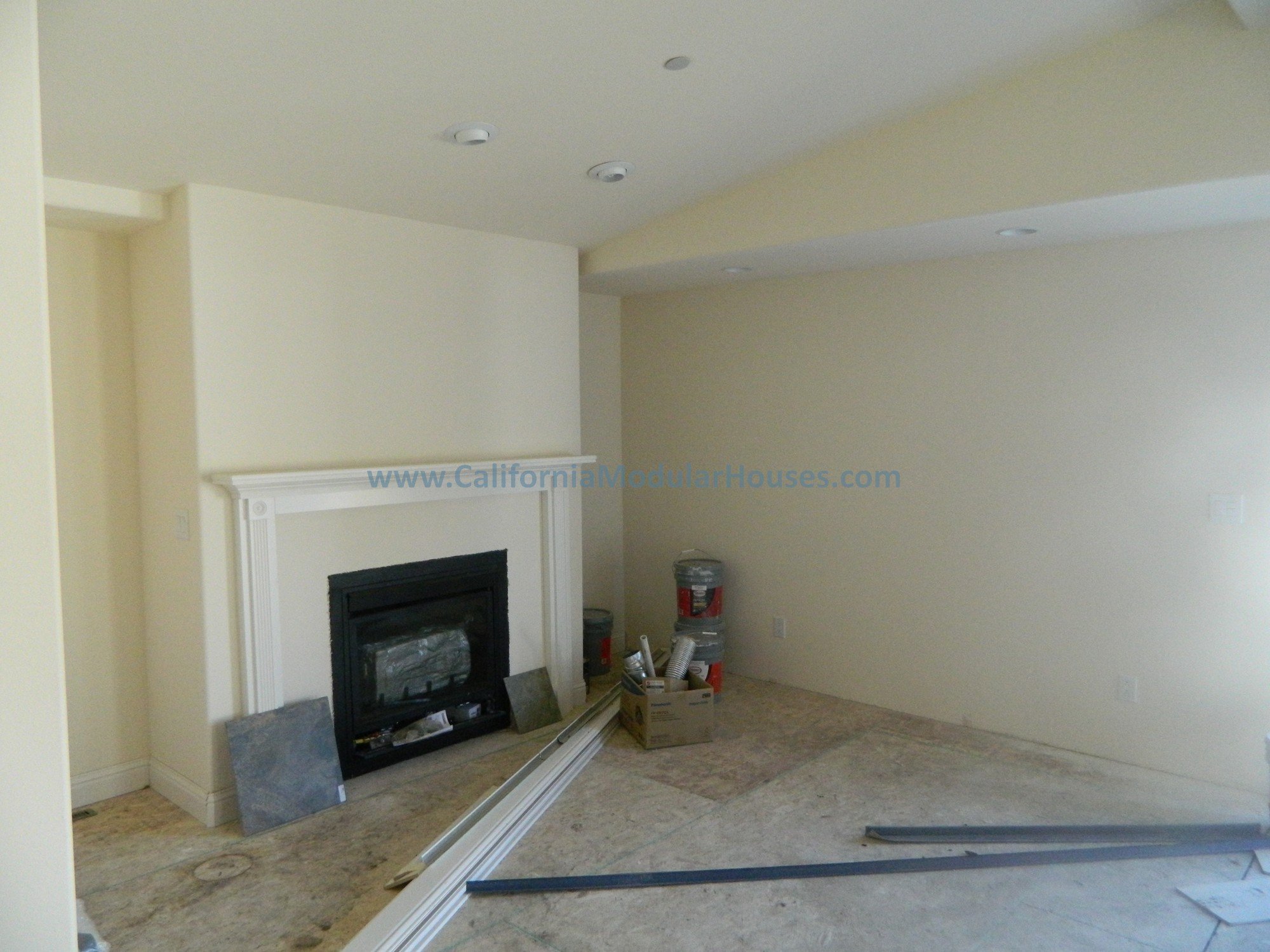 Living room under construction with a fireplace, construction materials, and tools on the floor.