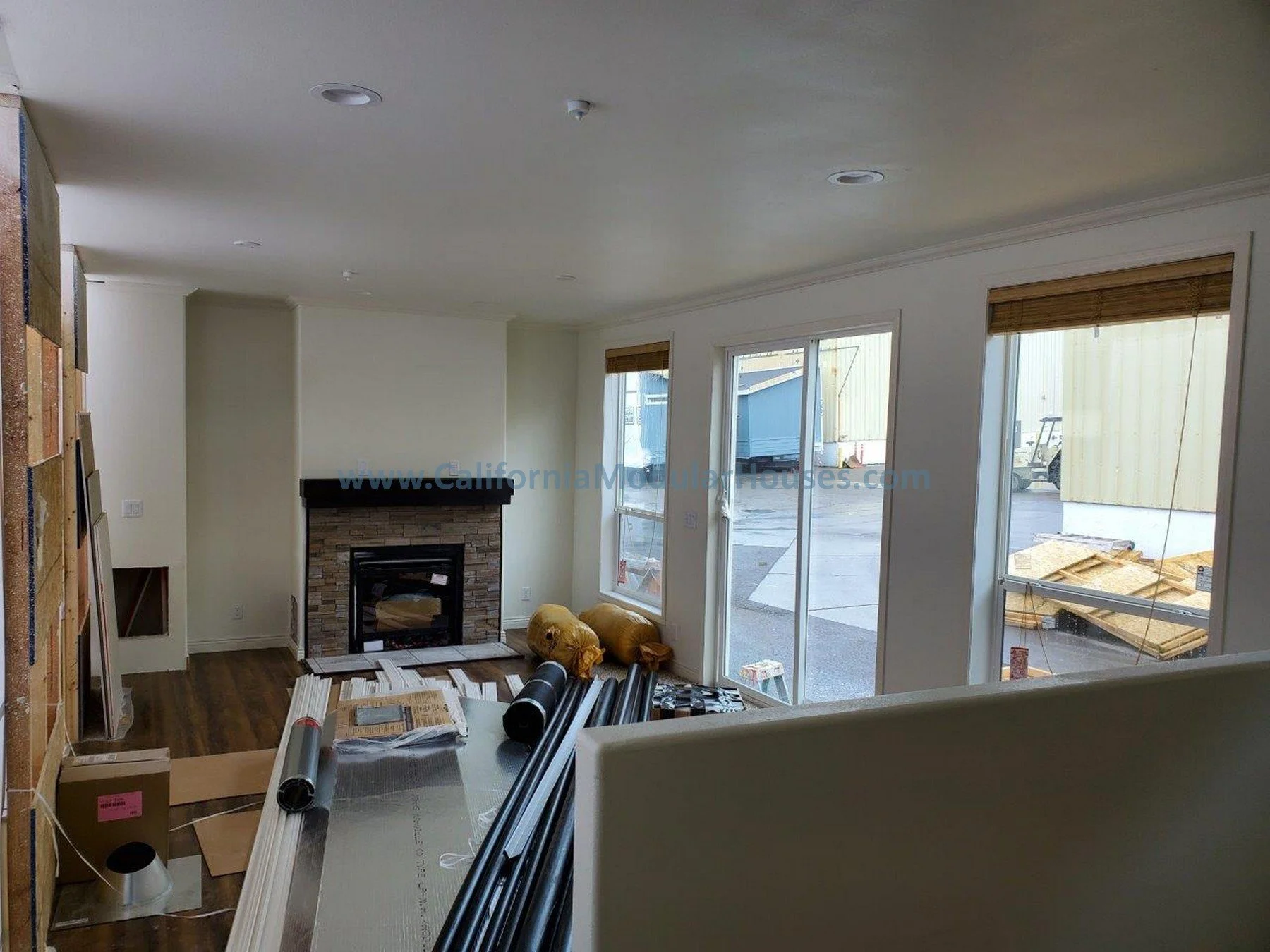 Interior of a house under construction with large windows, a fireplace, and construction materials on the floor.  City of Santa Barbara, Santa Barbara County, CA.   Modular Homes, California Modular,