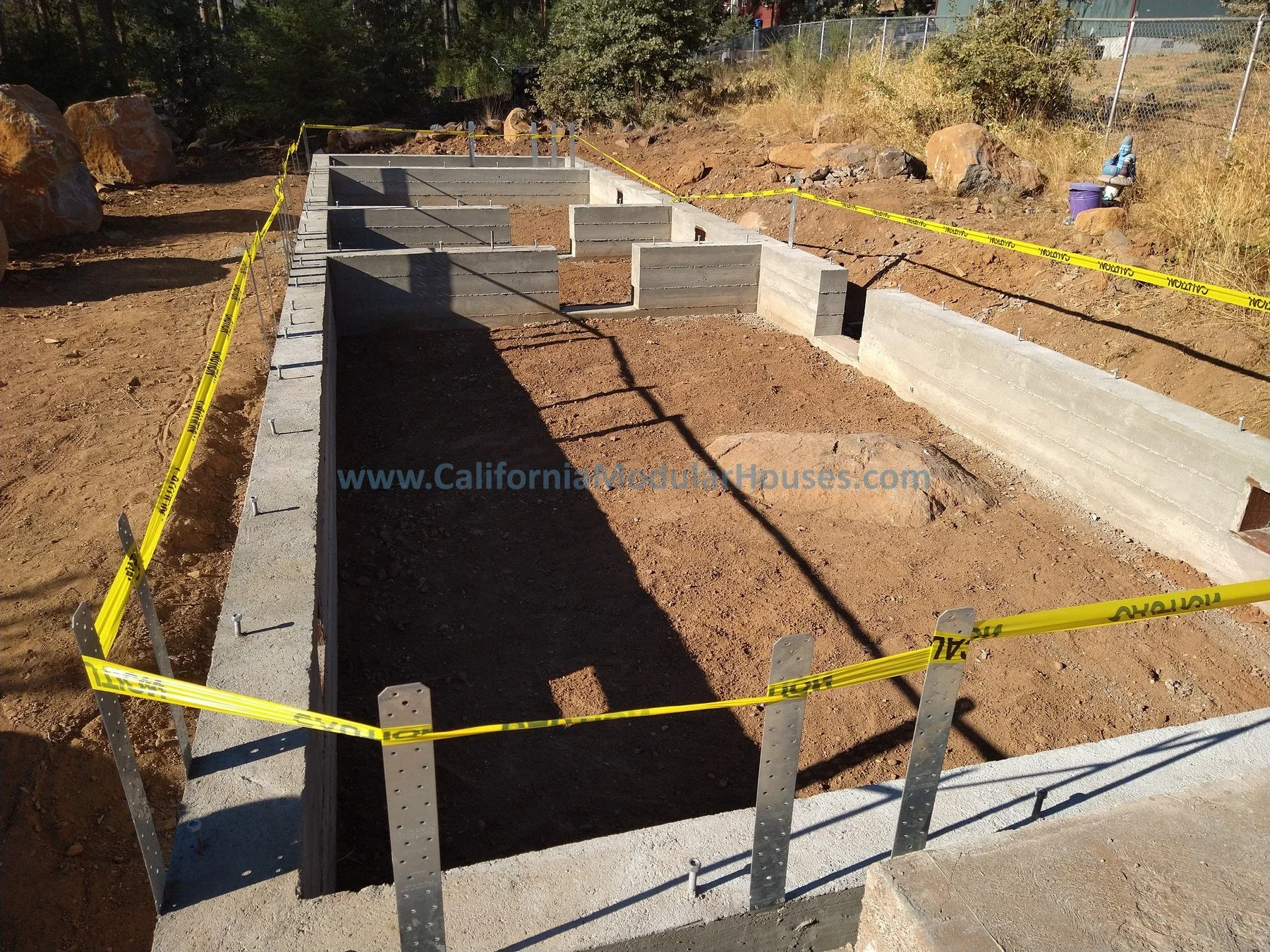 Construction site with foundation and concrete walls, yellow caution tape, and surrounding dirt ground.  California Modular Home, Modular Homes in California, Modular Homes Northern California, 