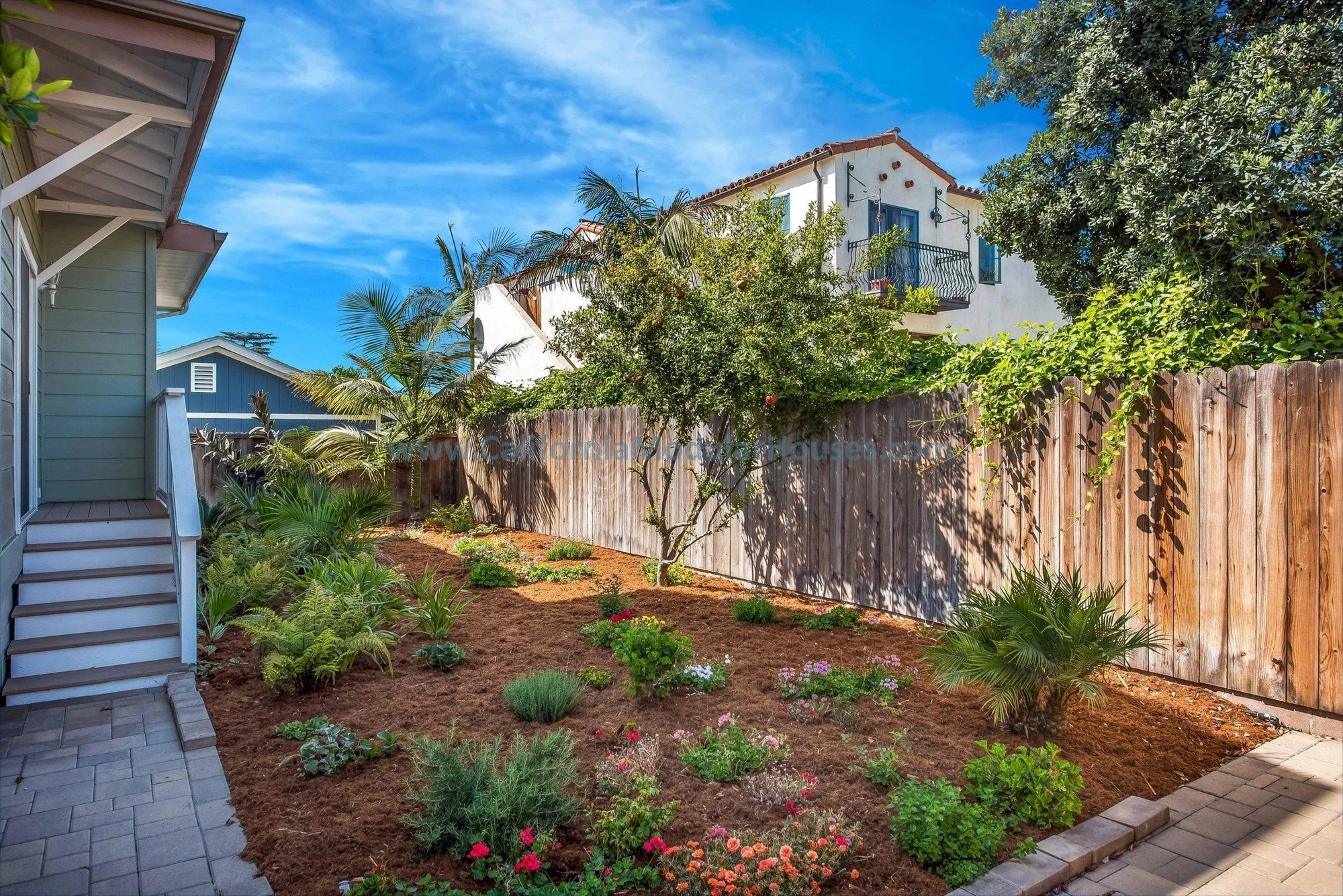 Backyard view of a sage green, brown trim prefab modular, two-story home. White door, white railing.