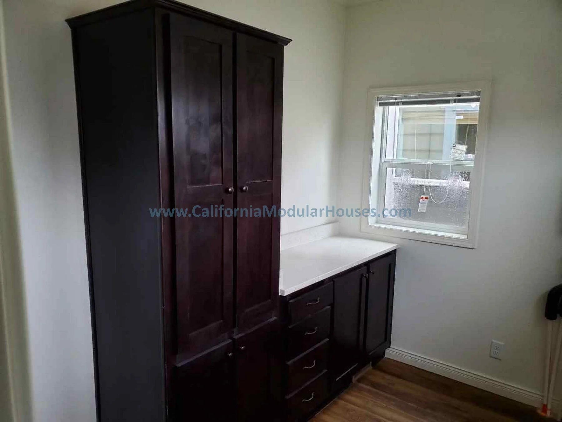 Interior of a small room with dark wooden cabinetry, a window with blinds, and hardwood flooring.  Modular Home on a Sloped Property.  Prefab Modular Homes California,