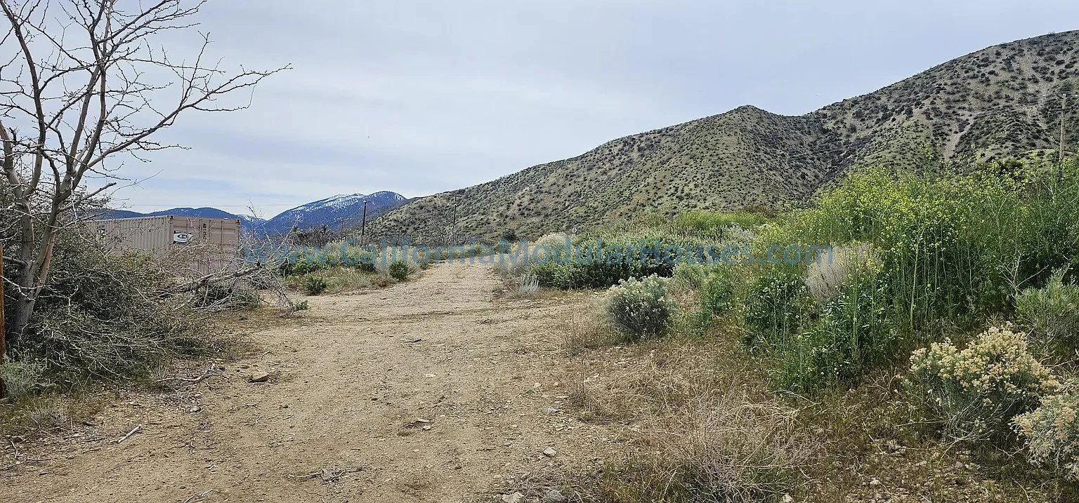 Dirt trail in a desert landscape with sparse vegetation, mountains in the background, and a cloudy sky.