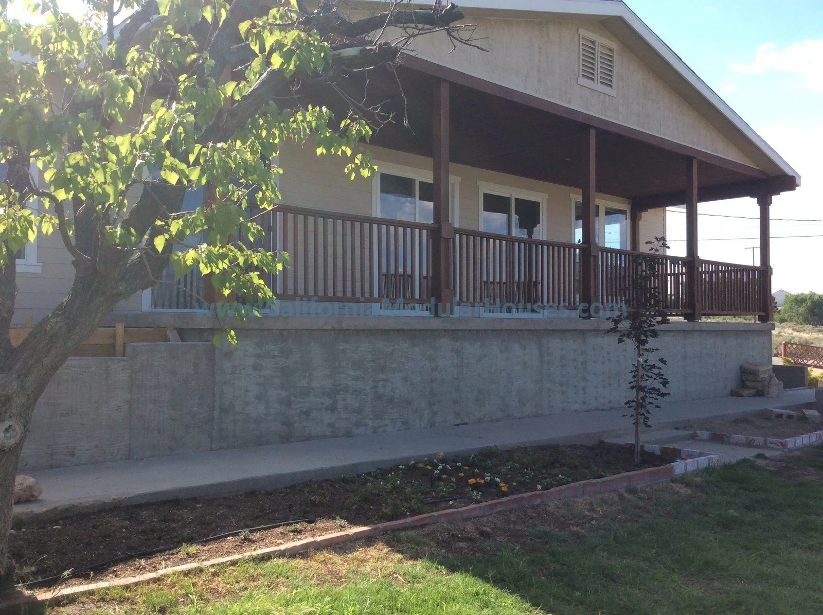 A house with a wooden balcony and railing, with trees and greenery in the front yard.
