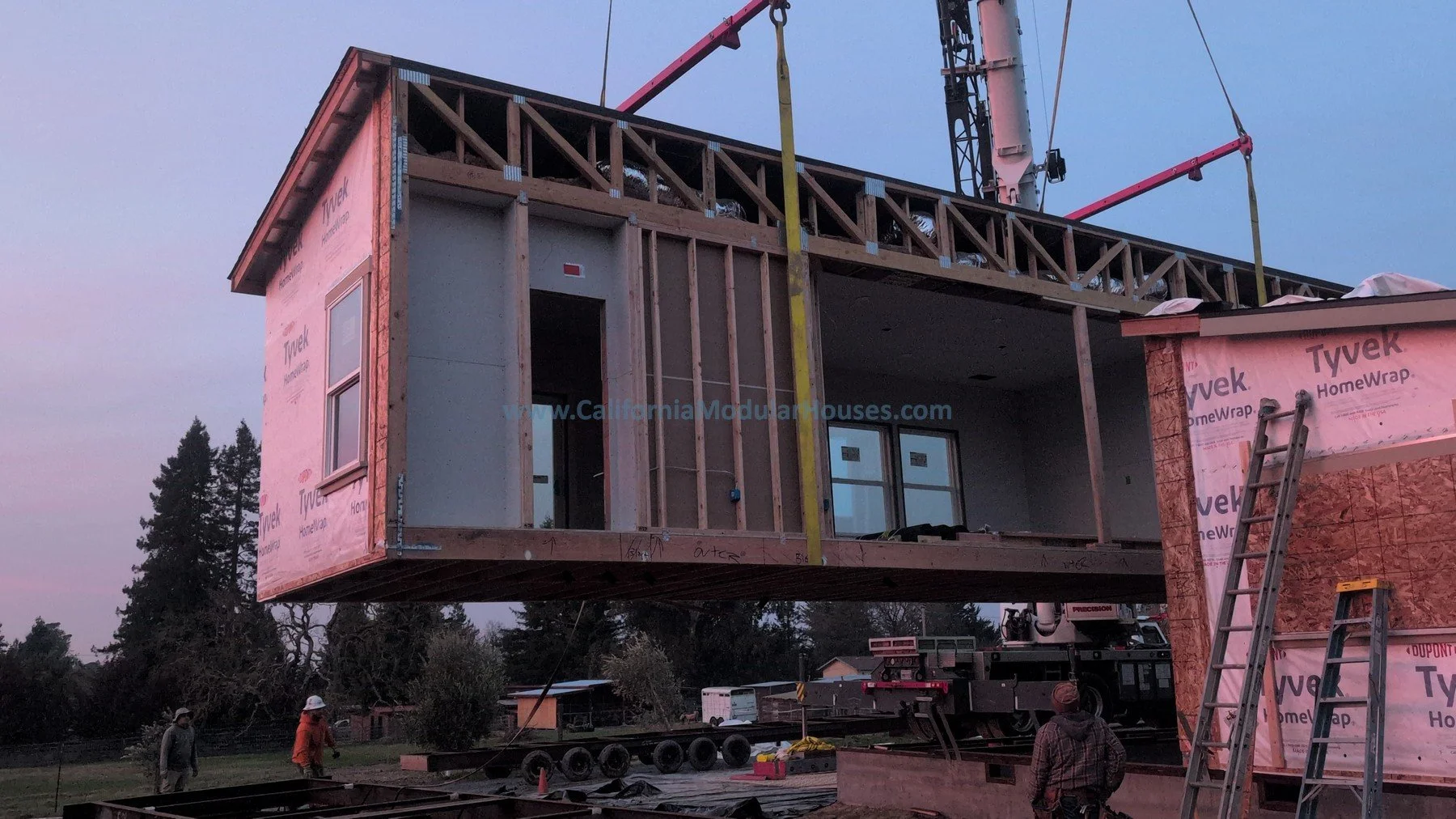 Under construction of a modular home with wooden framework, pink house wrap, and workers preparing for installation.  Sabastopol, CA.  Sonoma County, CA.  Pre-fab Modular Home.  ADU.  
