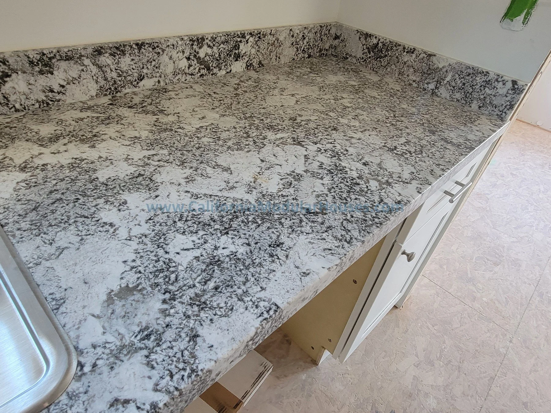 Granite countertop in a kitchen with white cabinetry and a stainless steel sink visible on the left.