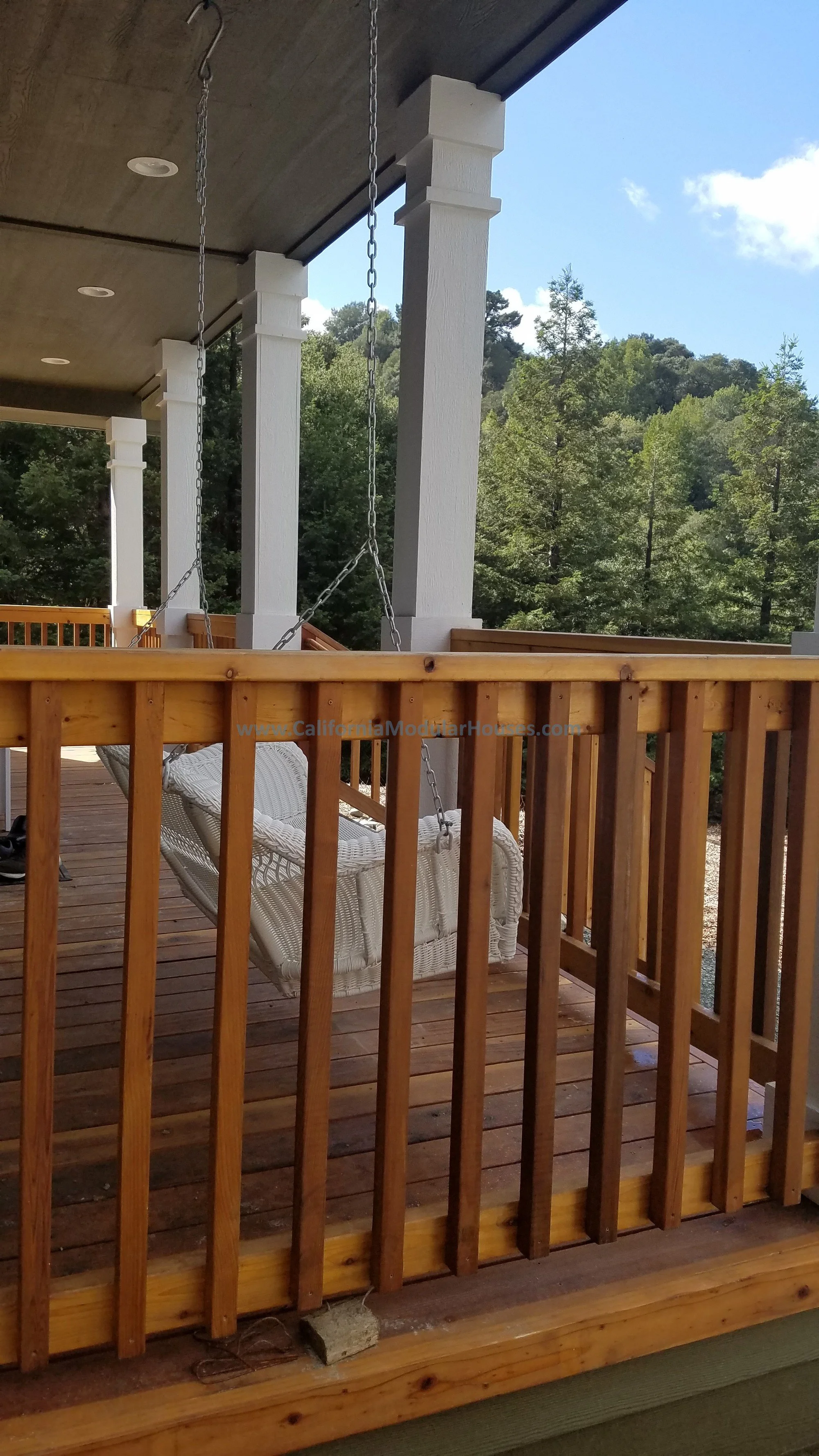 A wooden porch with a swing and a view of trees and hills in the background.  Who wouldn't want to sit on this and take in the view of the woods, sitting on the front porch swing.  Orinda, Contra Costa County, CA.  