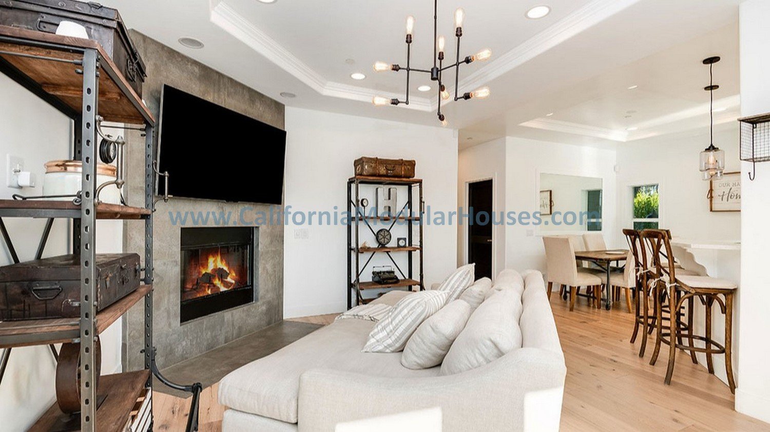 Living room with a fireplace, featuring a tray ceiling with recessed lights and fire sprinklers also showing a view of the kitchen making it a large open area in this modular home.  Custom designed modular home.  