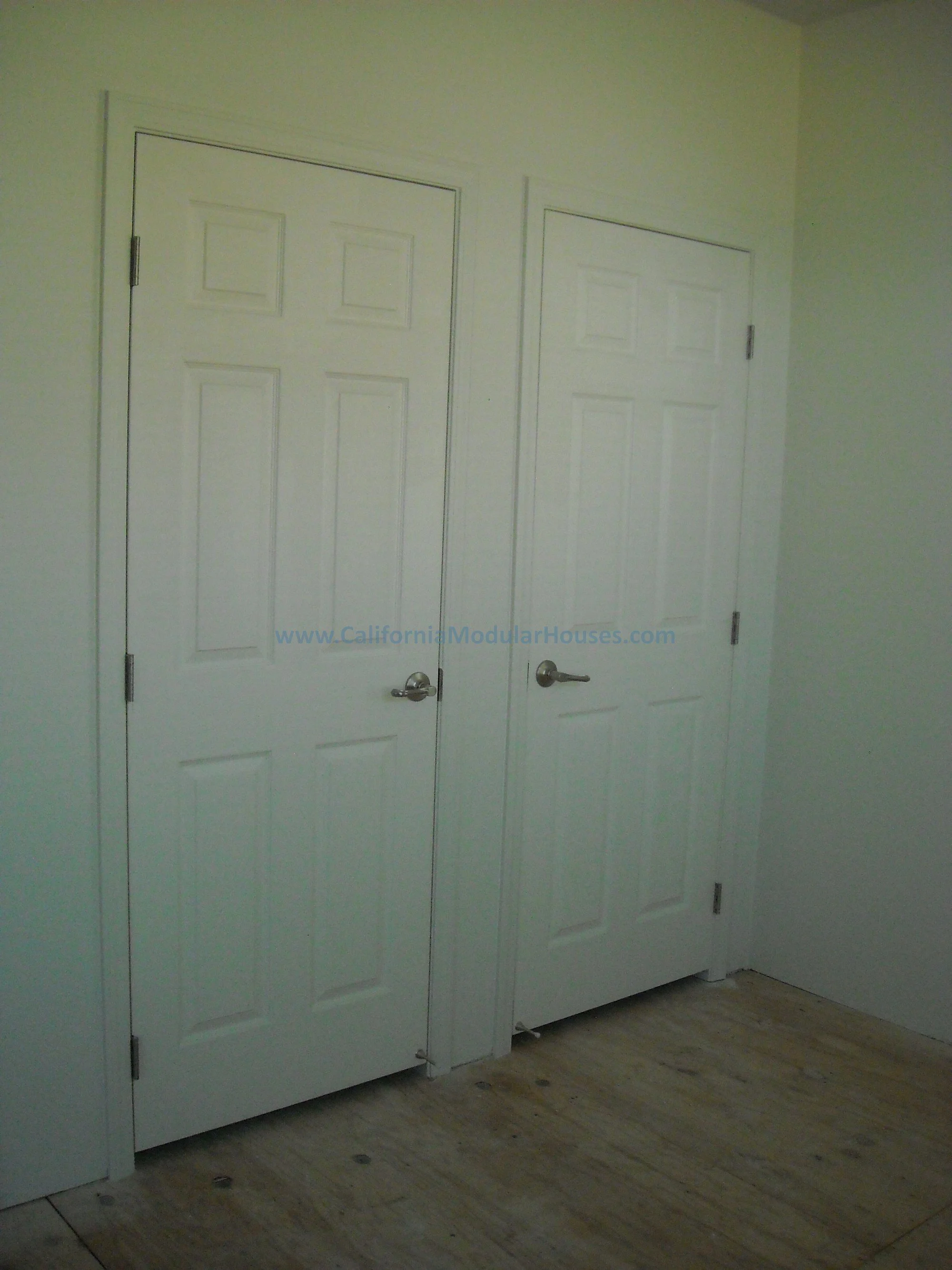 Two white interior doors with silver handles in a room with unfinished wooden flooring.  Factory Built Housing, California.  