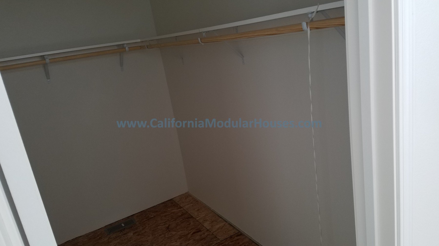 Large empty walk-in closet with beige walls, wooden shelf and a clothing rod, and a hardwood floor.  California Modular, California Modular Home,  Modular Homes,