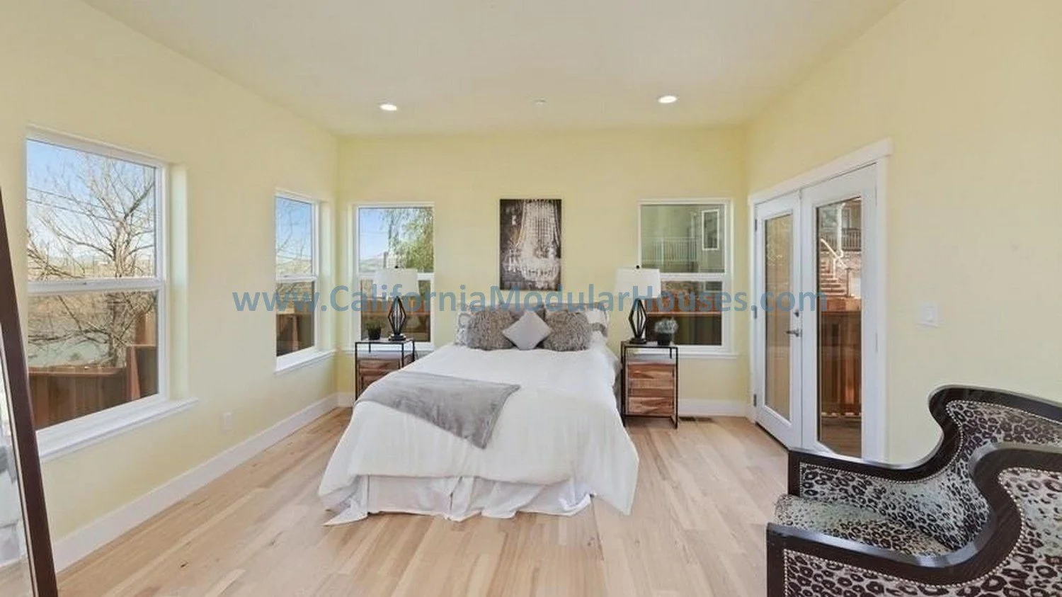 Bedroom with a bed, nightstands, windows, and a patterned chair.   California Modular Houses, Inc.    Modular house interior.  