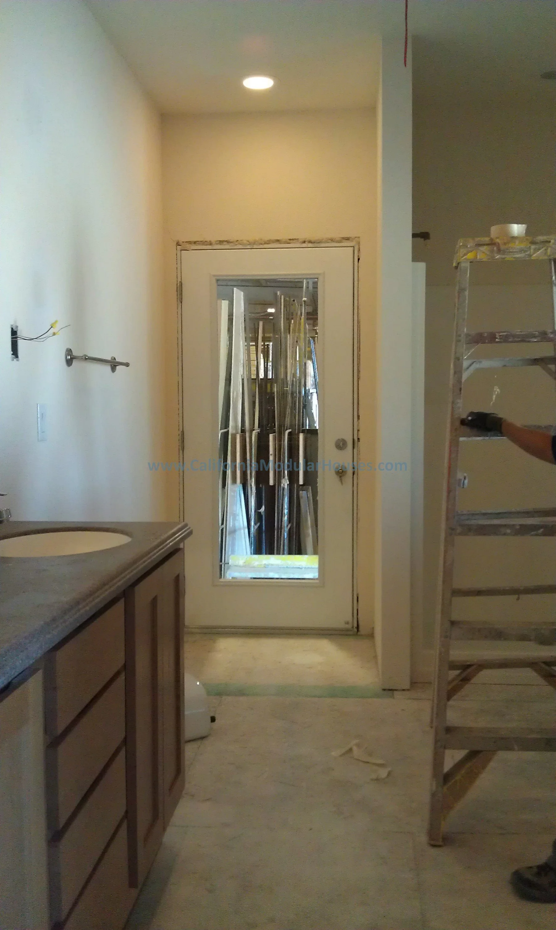 Kitchen area under renovation with cabinet on the left, ladder on the right, and a door with a mirror reflecting construction materials inside. Modular Homes California, Prefab Home California.
