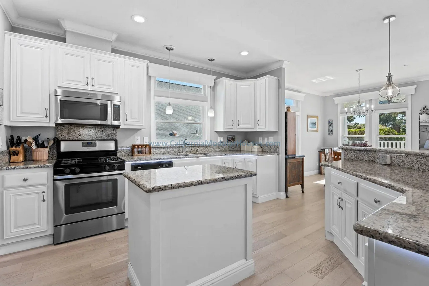 Modular prefab house. California. Cape Cod home with attic finished on-site. Bright kitchen with white cabinets, granite countertops, stainless steel stove and microwave, hardwood floors, and large windows with natural light.