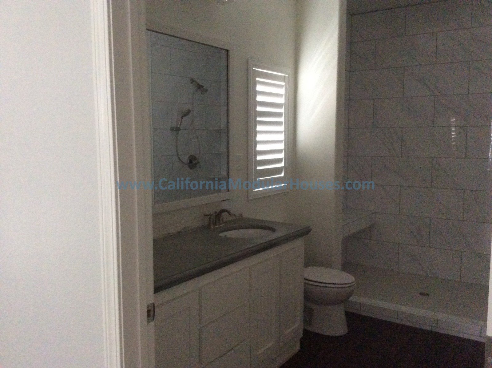 Bathroom with a vanity, a mirror, a toilet, and a walk-in shower with gray tiles, a window with blinds, and beige walls.