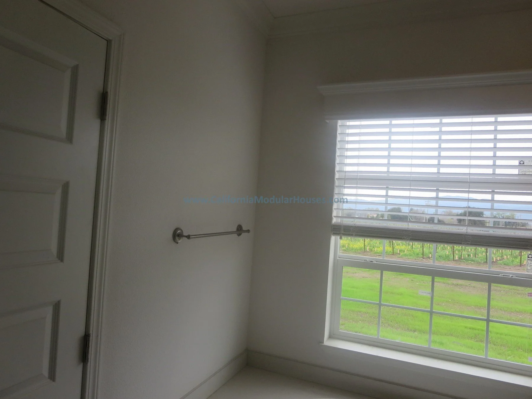 Room room with a window and blinds, a towel bar on the wall, and a closed door.  Modulars.   Napa, CA.  Prefab.  California Modular House. California modular home.  Modulars.  