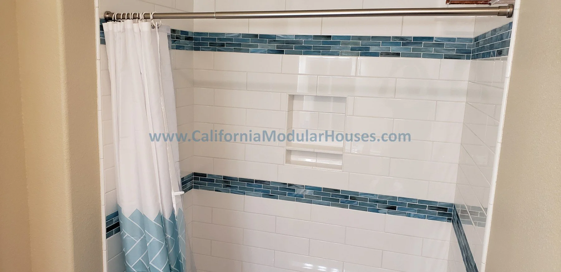 A tiled shower with a white curtain featuring a geometric design, blue tile accents, and a built-in niche for shower products.  Interior Modular Prefab ADU Photograph  Kenwood, Sonoma County, CA. 