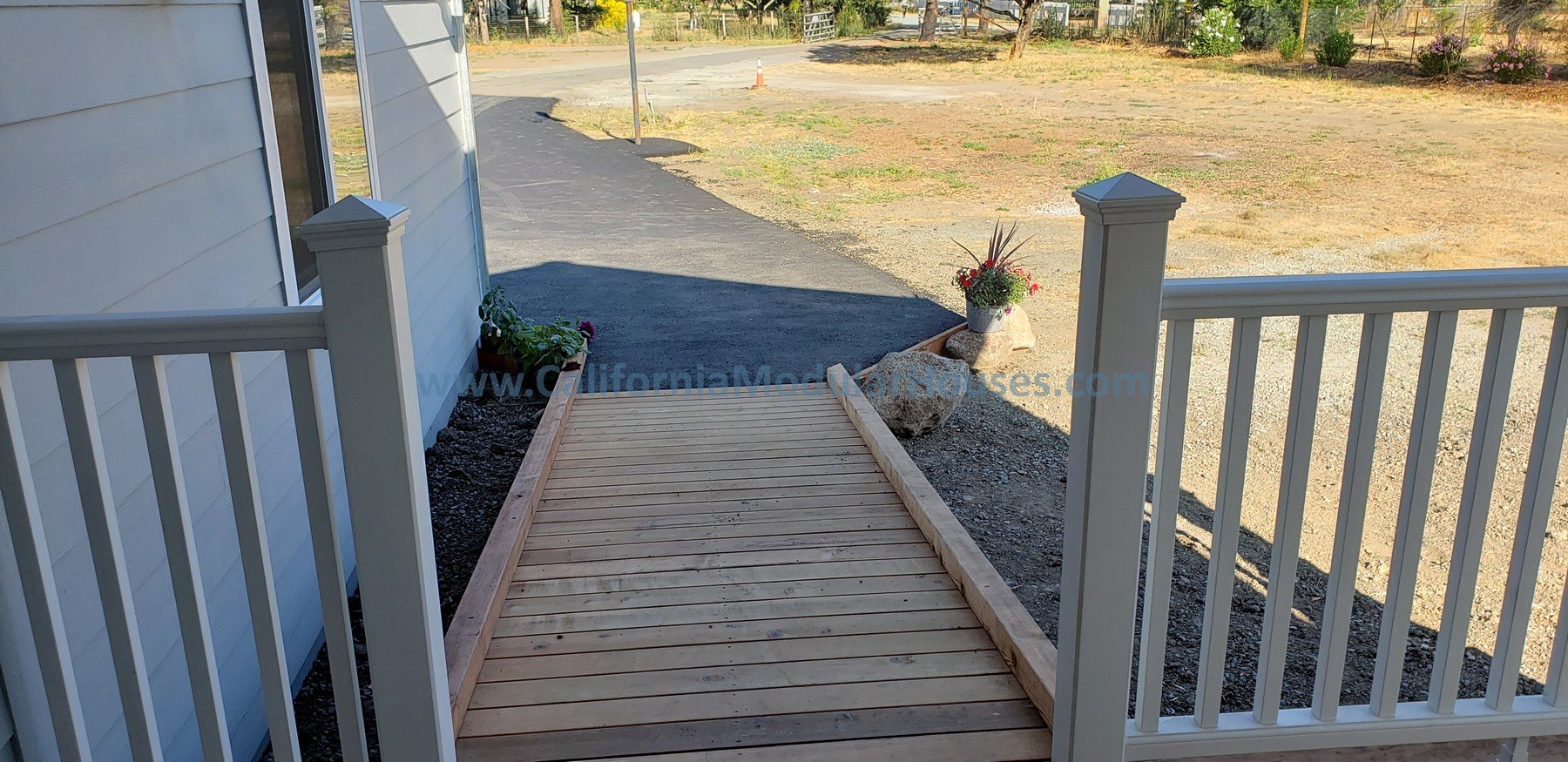 Front porch with wooden wheelchair ramp and flower pots on either side, overlooking a natural yard and street.  Kenwood, Sonoma County, CA.  Prefab Modular ADU