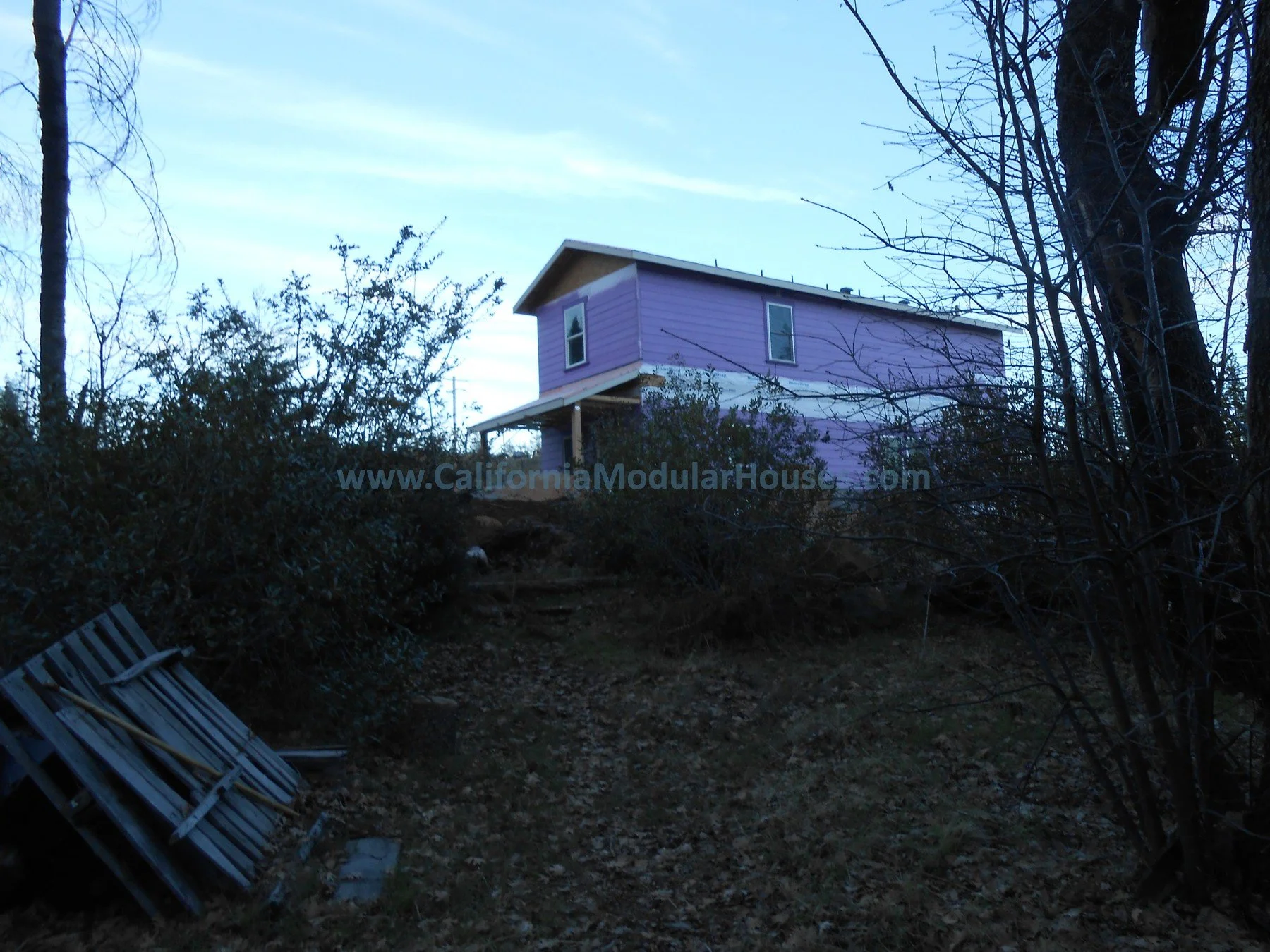 A purple modular house on stilts situated on a hilltop with leafless trees and bushes around, under a blue sky.  California Modular Home,  Modular Homes, Modular Homes California, Lake County, CA.  