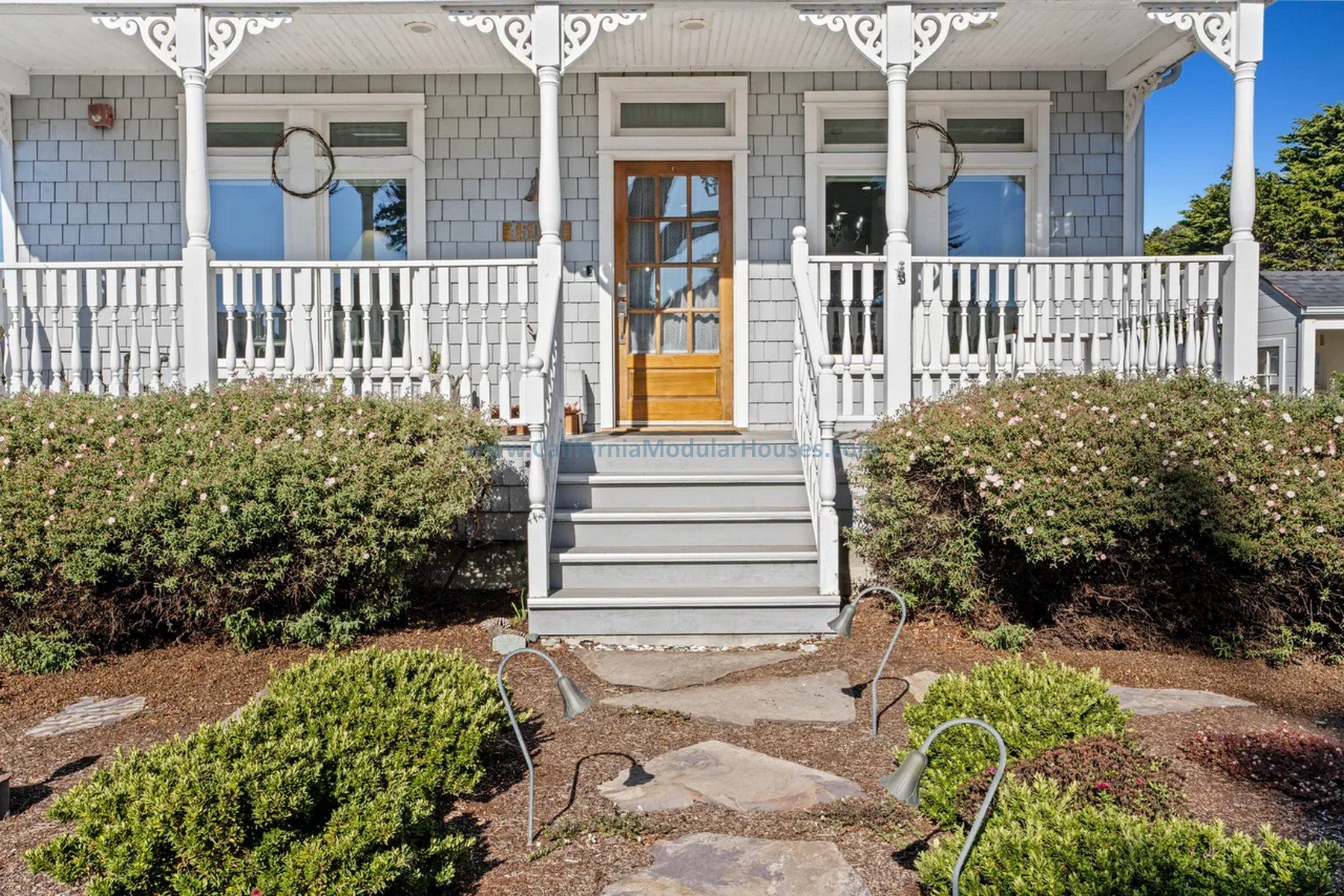 Front view of a small, light gray, Victorian-style house with a wooden door, white porch railings, and stairs leading up to the entrance.   Unfinished attic.  Prefab Modular Home for Northern California Coast.  Modulars.  California modular.