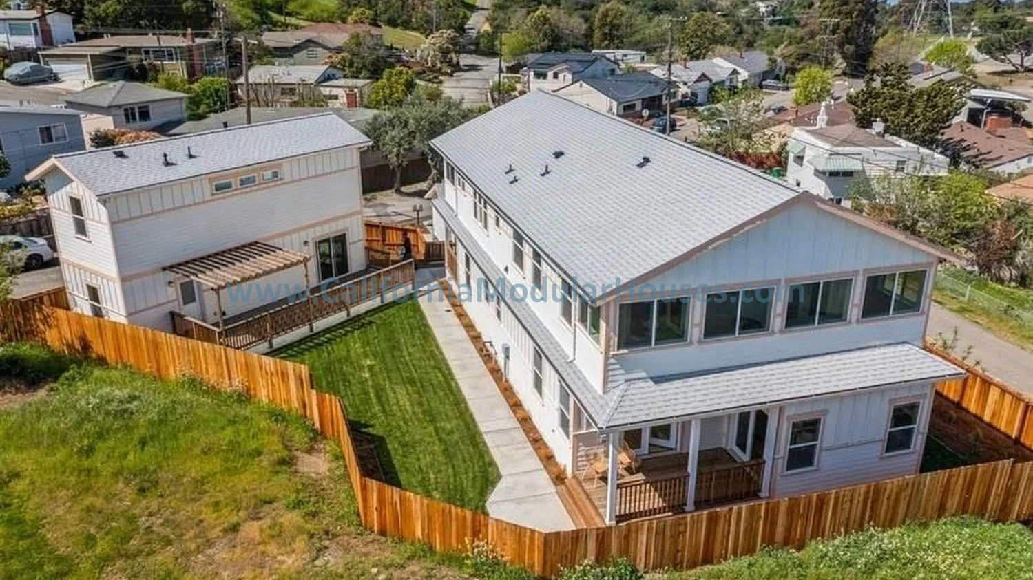 Aerial view of two modern white houses with metal roofs, surrounded by a wooden fence.  California prefab modular home.  Contra Costa County.  