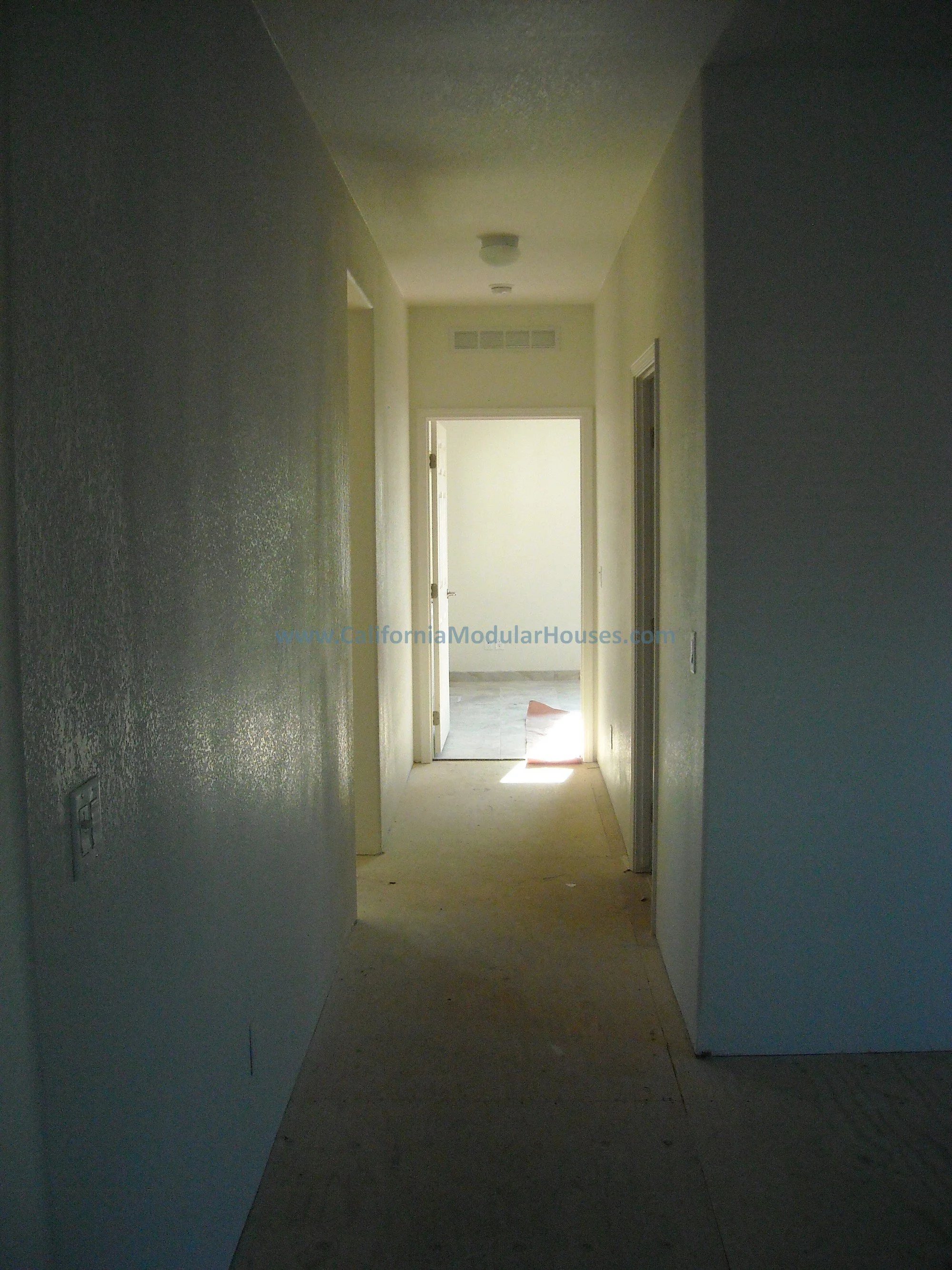 Empty hallway in a house under construction with open doors and natural light at the end of this modular home near Lake Isabella in Central California.  