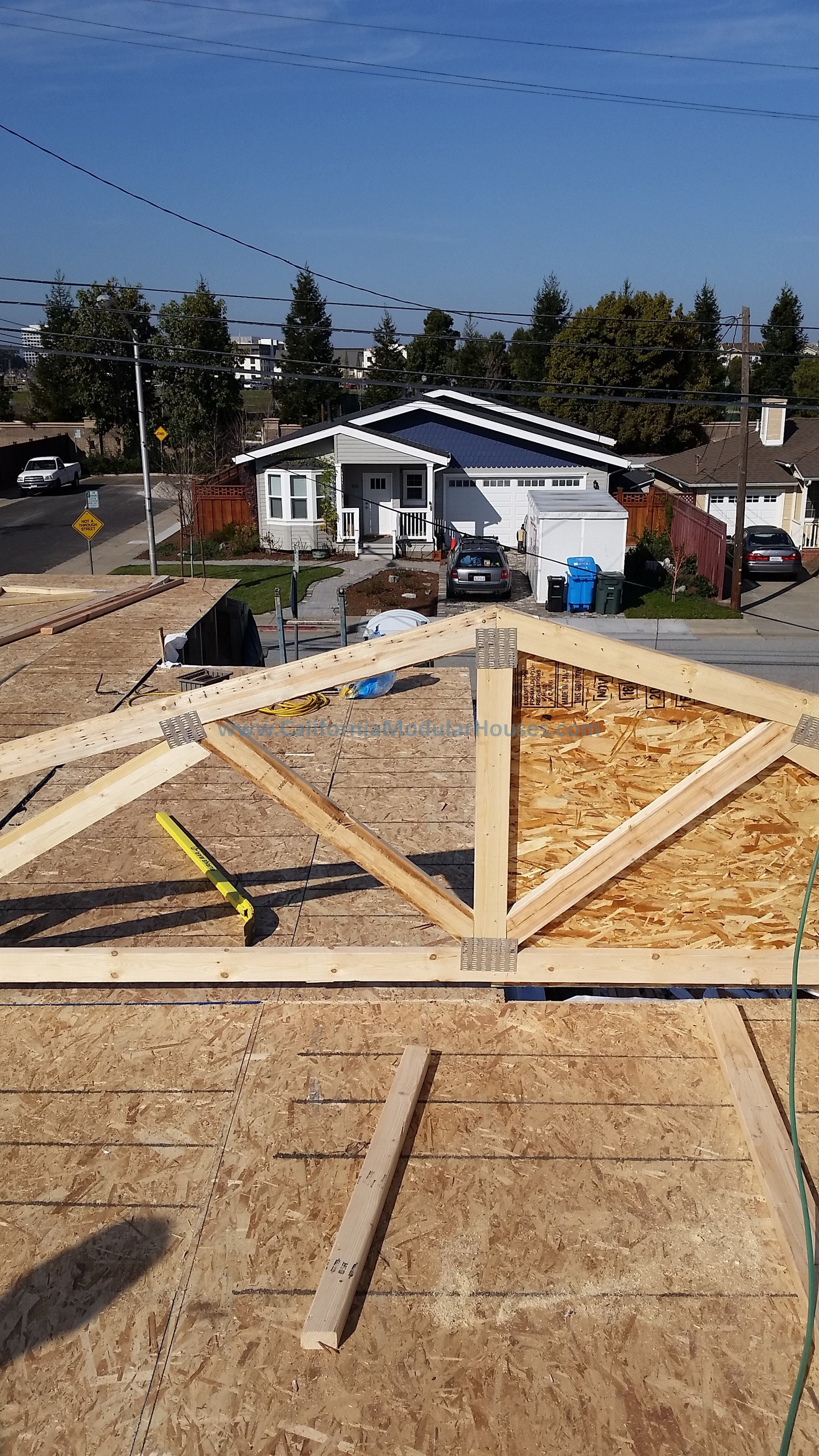 View from roof under construction showing wooden framing and OSB sheathing, with neighboring houses and a street in the background.  California Modular Houses,  San Mateo Modular Home.