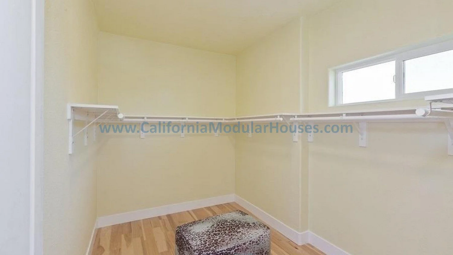 Empty walk-in closet with yellow walls, a small window, white shelves, and a leopard print ottoman on a wooden floor.  PreFab Modular for California.  Contra Costa County 2 story modular home.  Modular house. 