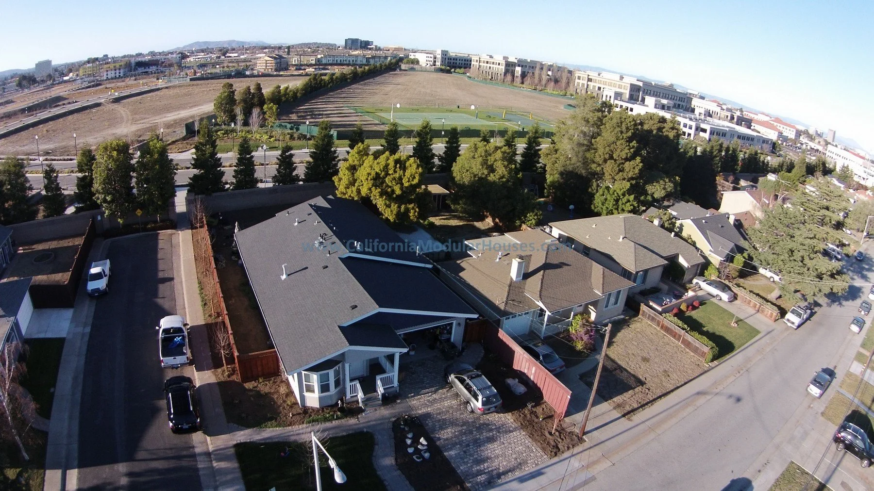 Aerial view of residential houses and a park with tennis courts, trees, and open fields in the background.  San Francisco Bay Area, CA.  City of San Mateo, San Mateo County, CA.  Prefab Home California, Pre-Fabricated Homes,