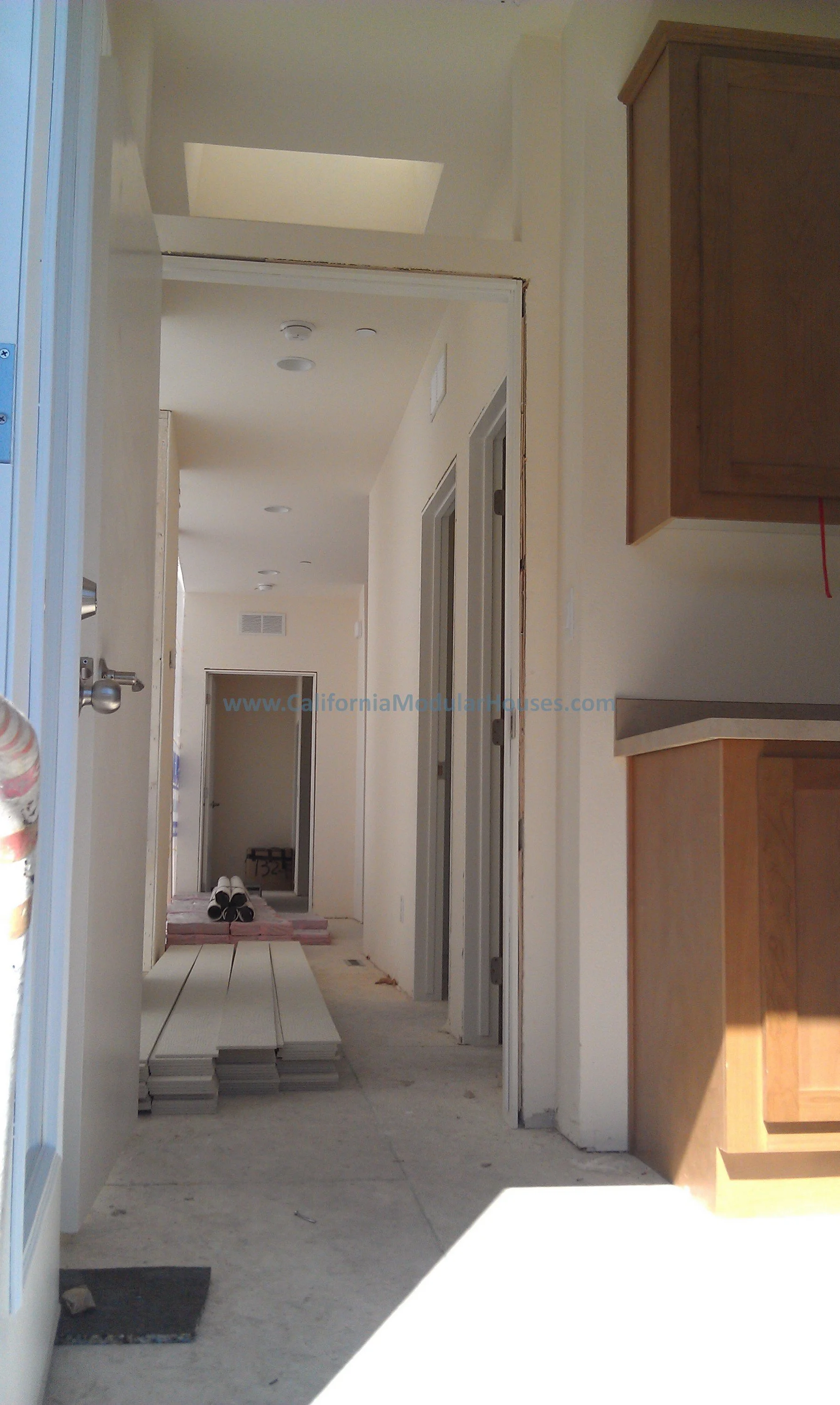 Hallway under construction with stacks of flooring materials, door frames, and partially installed cabinets.  California Modular Home, Modular Homes California.