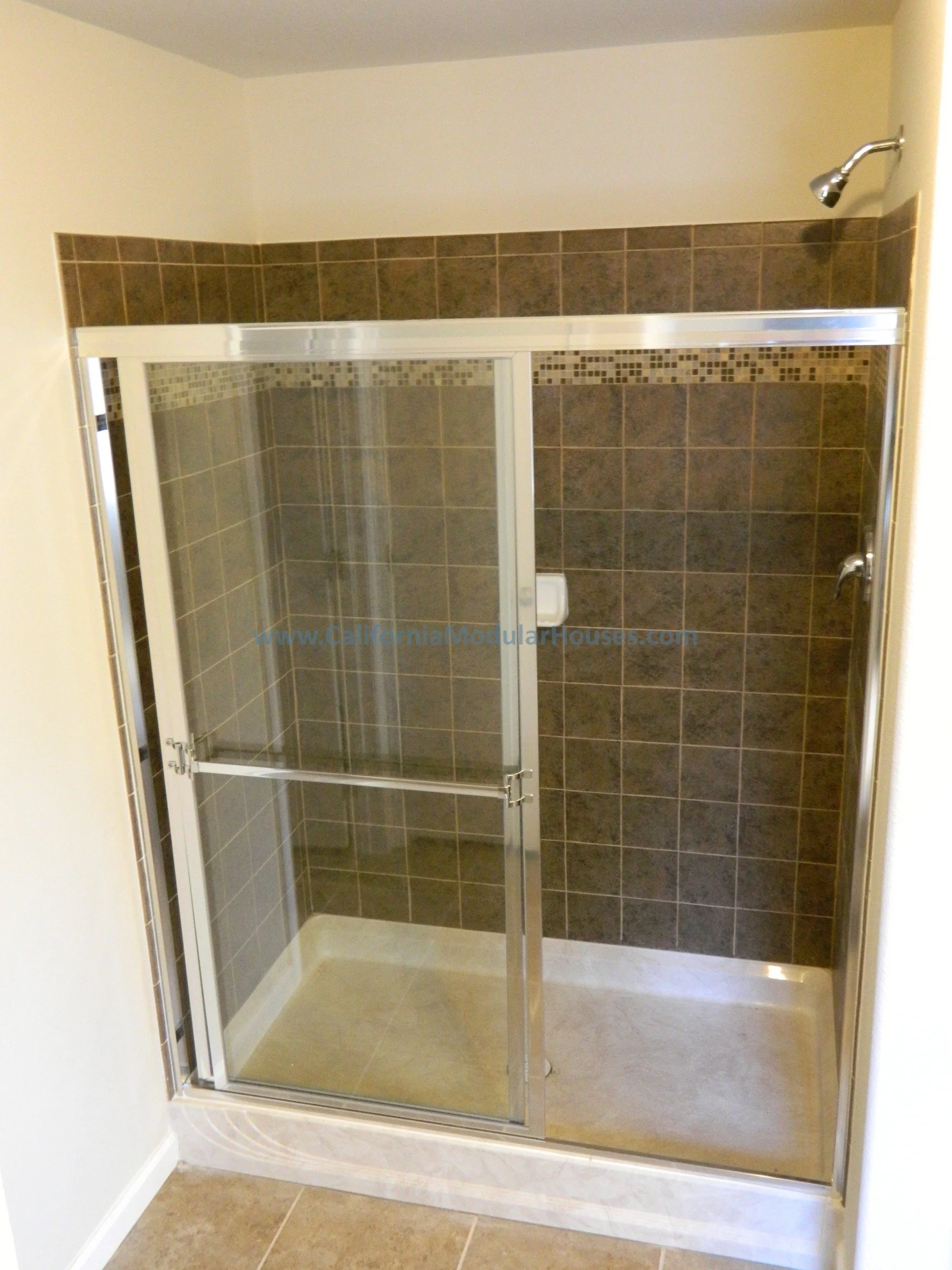 Bathroom shower with brown tiled walls, clear glass sliding doors, and a chrome showerhead.