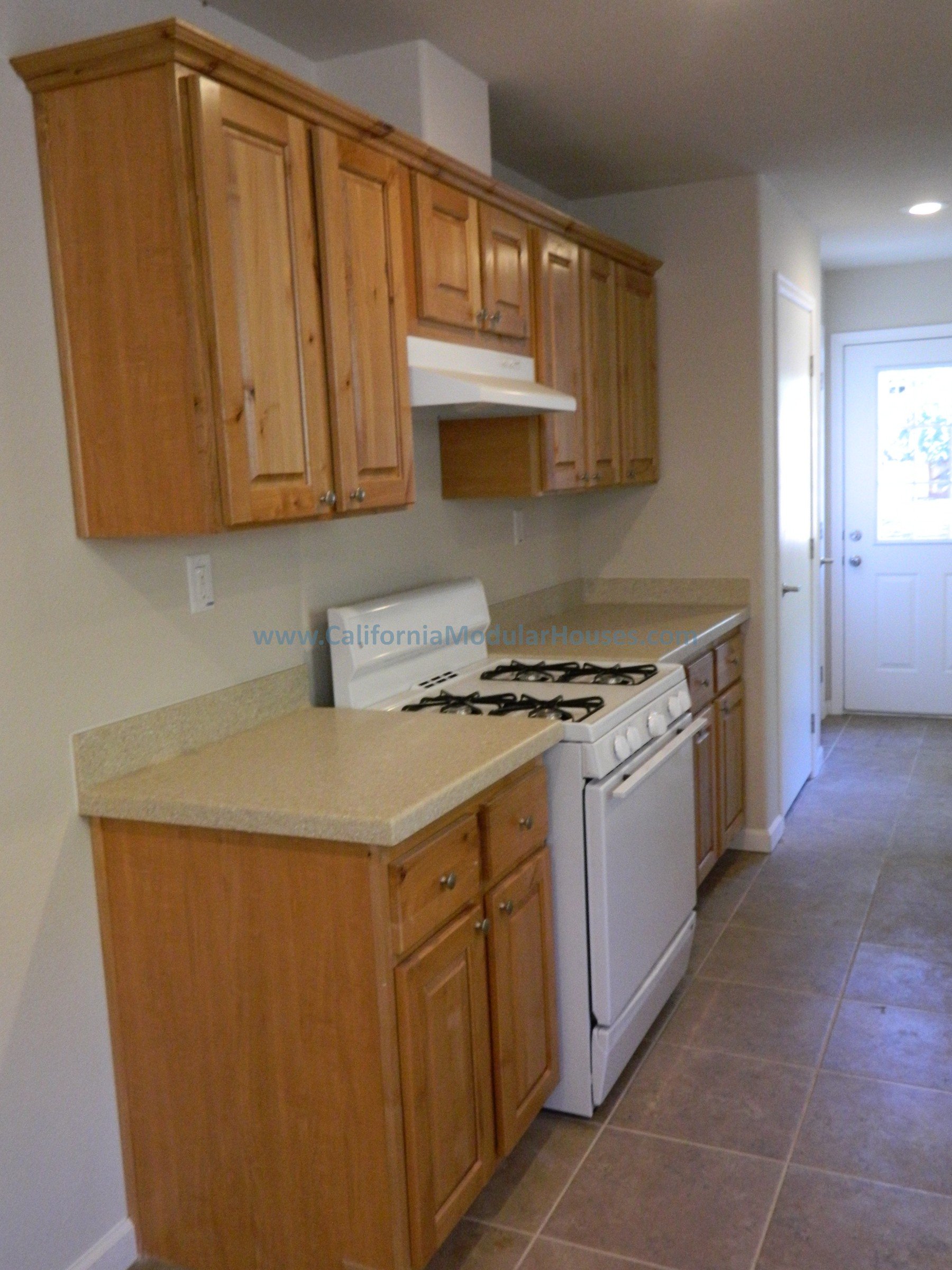 Kitchen with wooden cabinets, beige countertops, and a white gas stove with oven, located near a door leading outside.