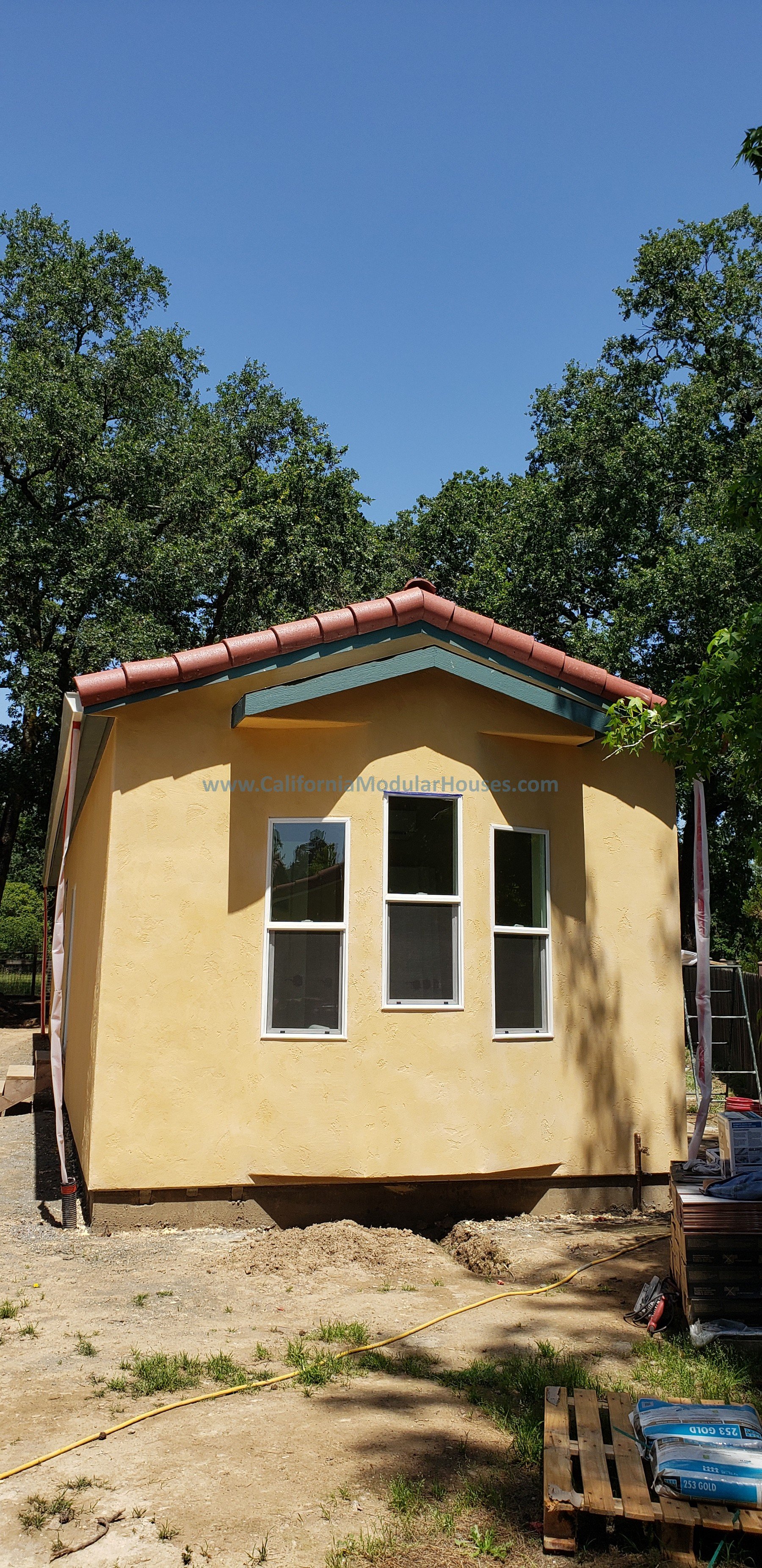 New yellow ADU house with three windows and a red-tiled roof, surrounded by trees.  Accessory Dwelling Unit for Healdsburg, CA.  Sonoma County Modular Accessory Dwelling Unit.  