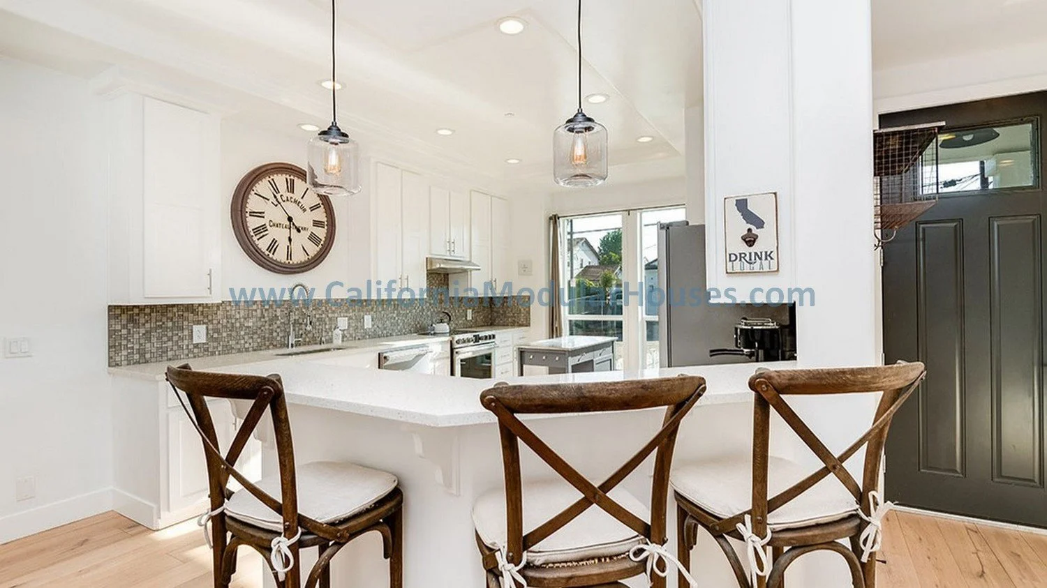 Modern kitchen with white cabinets, mosaic tile backsplash, large clock on the wall, and three wooden barstools with cushions at the island counter. A door and windows lead outside.  Modular Home with Peninsula island for seating.  