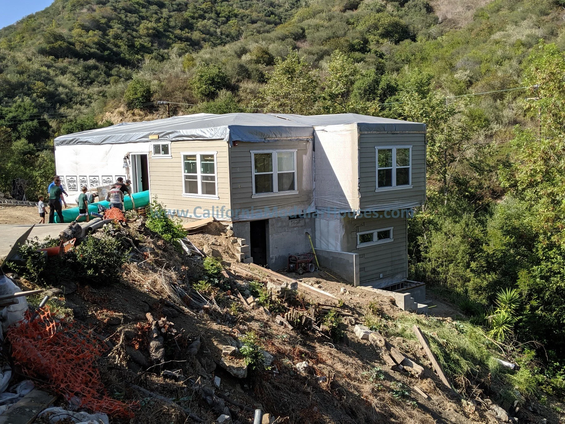 A house under construction on a hillside with workers installing the exterior siding, surrounded by trees.  Modular Homes California, Modular Homes in California, Prefab Home California, Pre-Fabricated Homes,