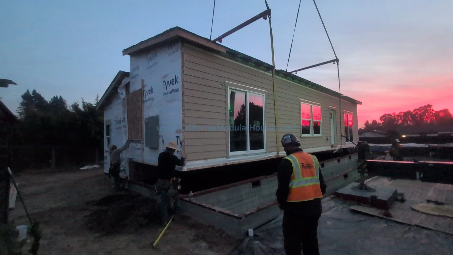 Sebastopol, Sonoma County, CA.  Prefab modular Accessory Dwelling Unit.  Construction workers installing a modular home on a foundation during sunset.