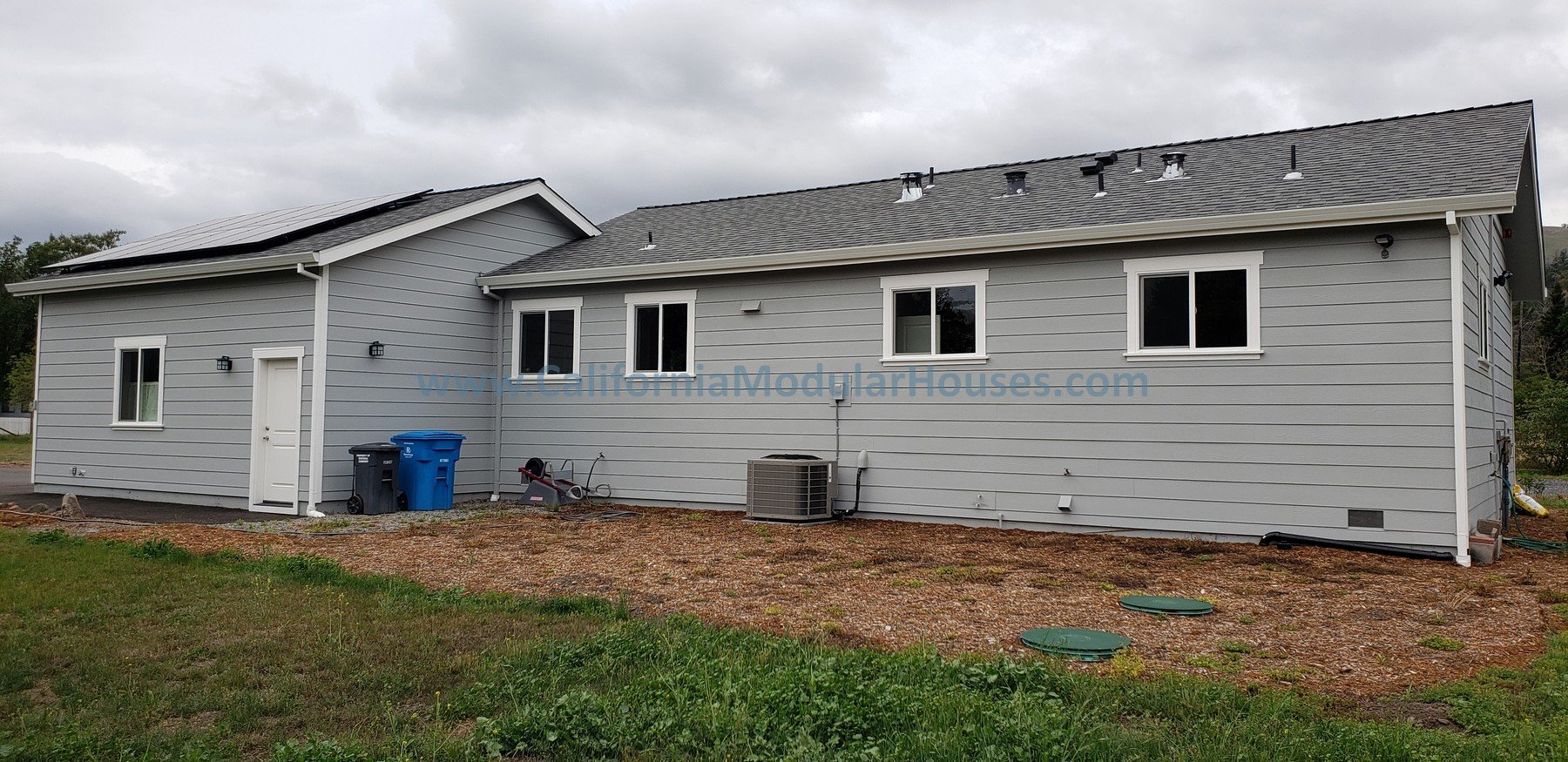 Side view of a one-story gray house with a sloped roof and multiple windows, on a cloudy day.  2 bedroom, 2 bathroom modular ADU from the exterior.   Kenwood, Sonoma County, CA. 