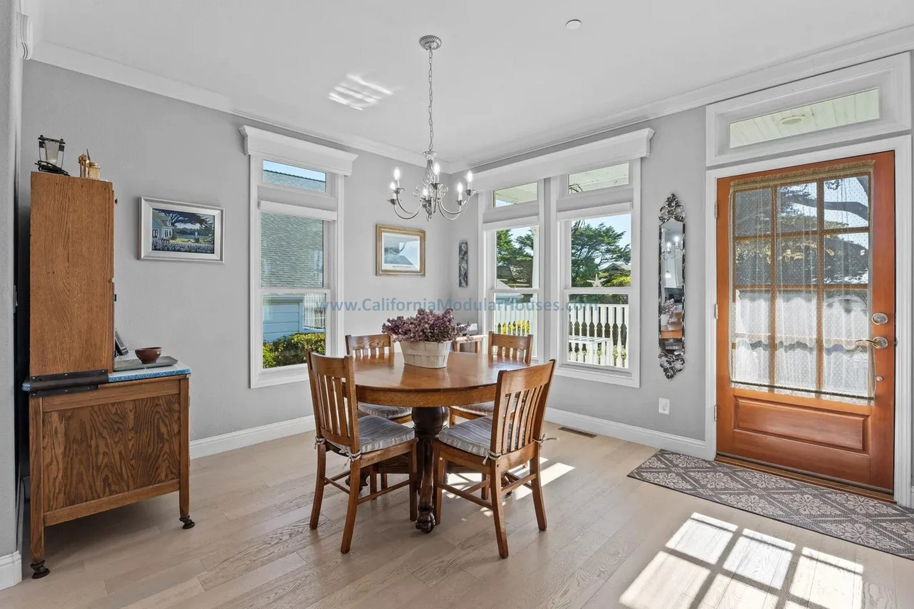 Dining room with a wooden table and four chairs, large windows, a chandelier, a wooden door with glass, a mirror.  California. Pre-fab modulars. Custom design coastal commission cape cod modular home.