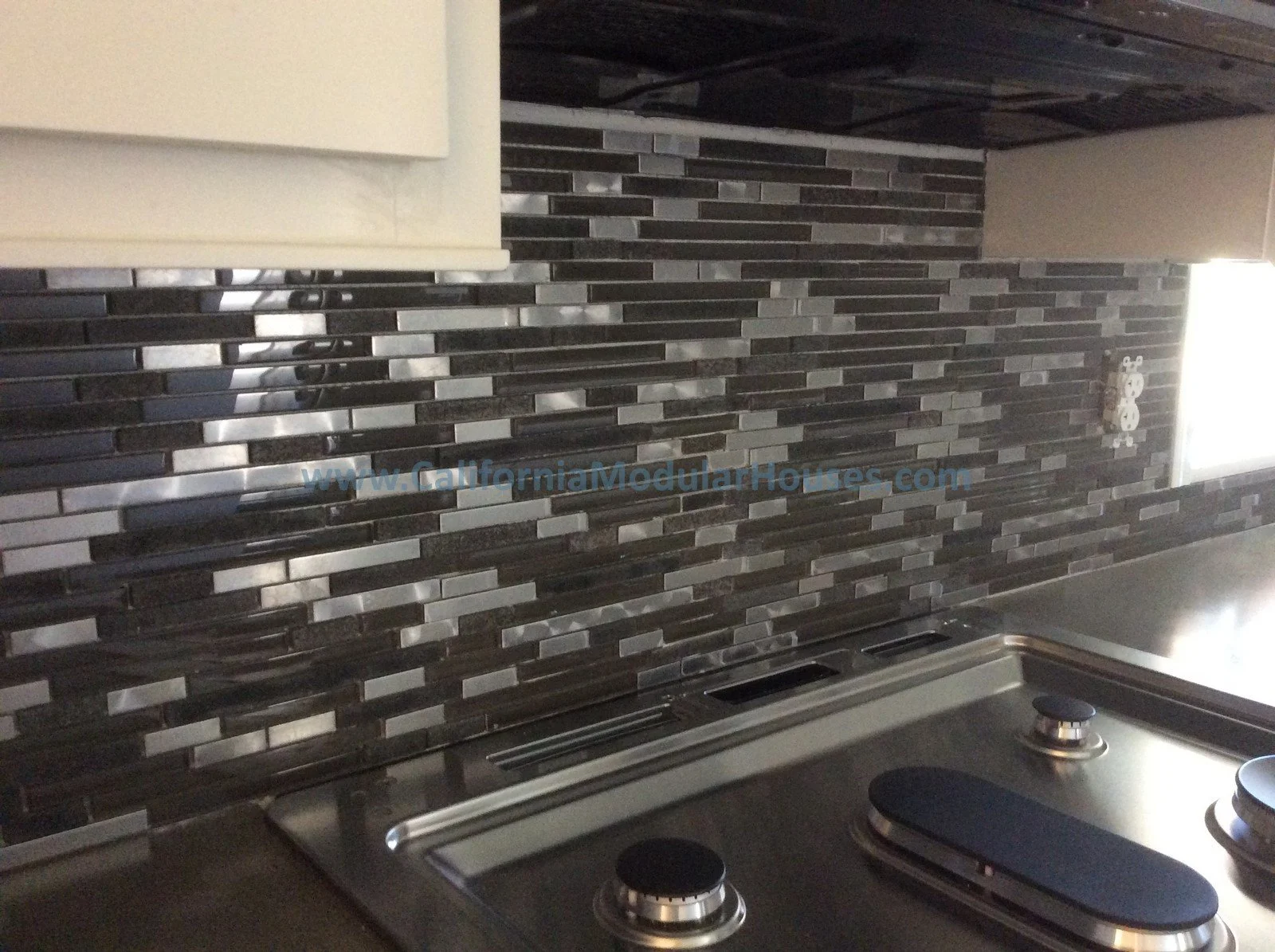 Modern kitchen backsplash with black and gray tiles above a stainless steel stovetop.